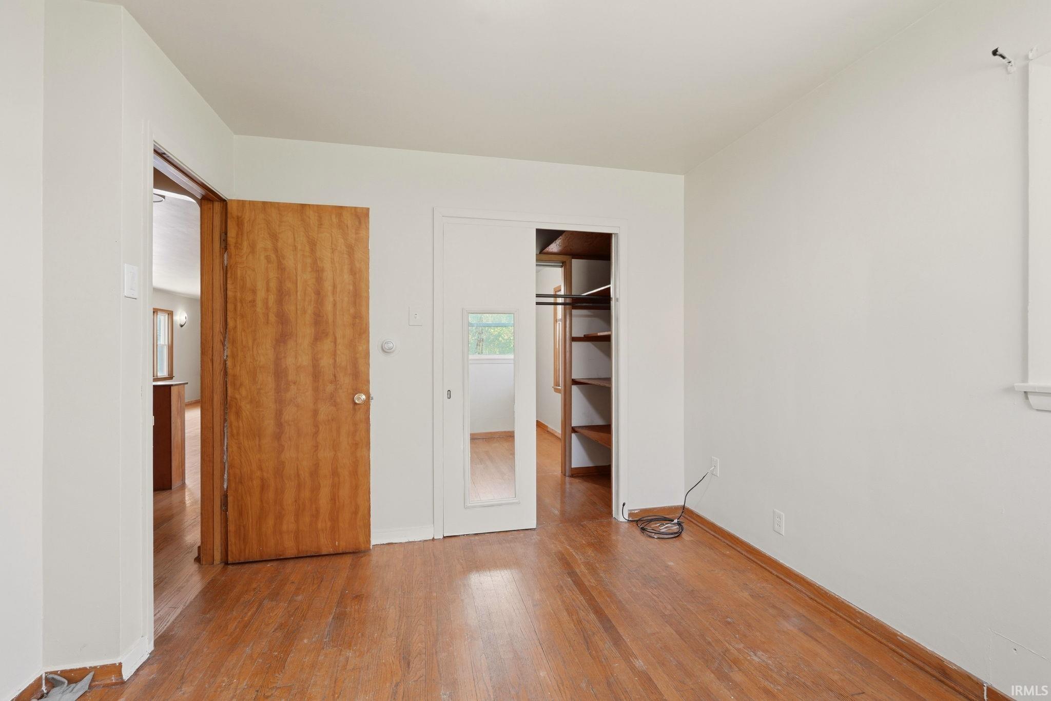Room with wood-finish flooring, white walls, and a built-in closet with shelving and a hanging rod