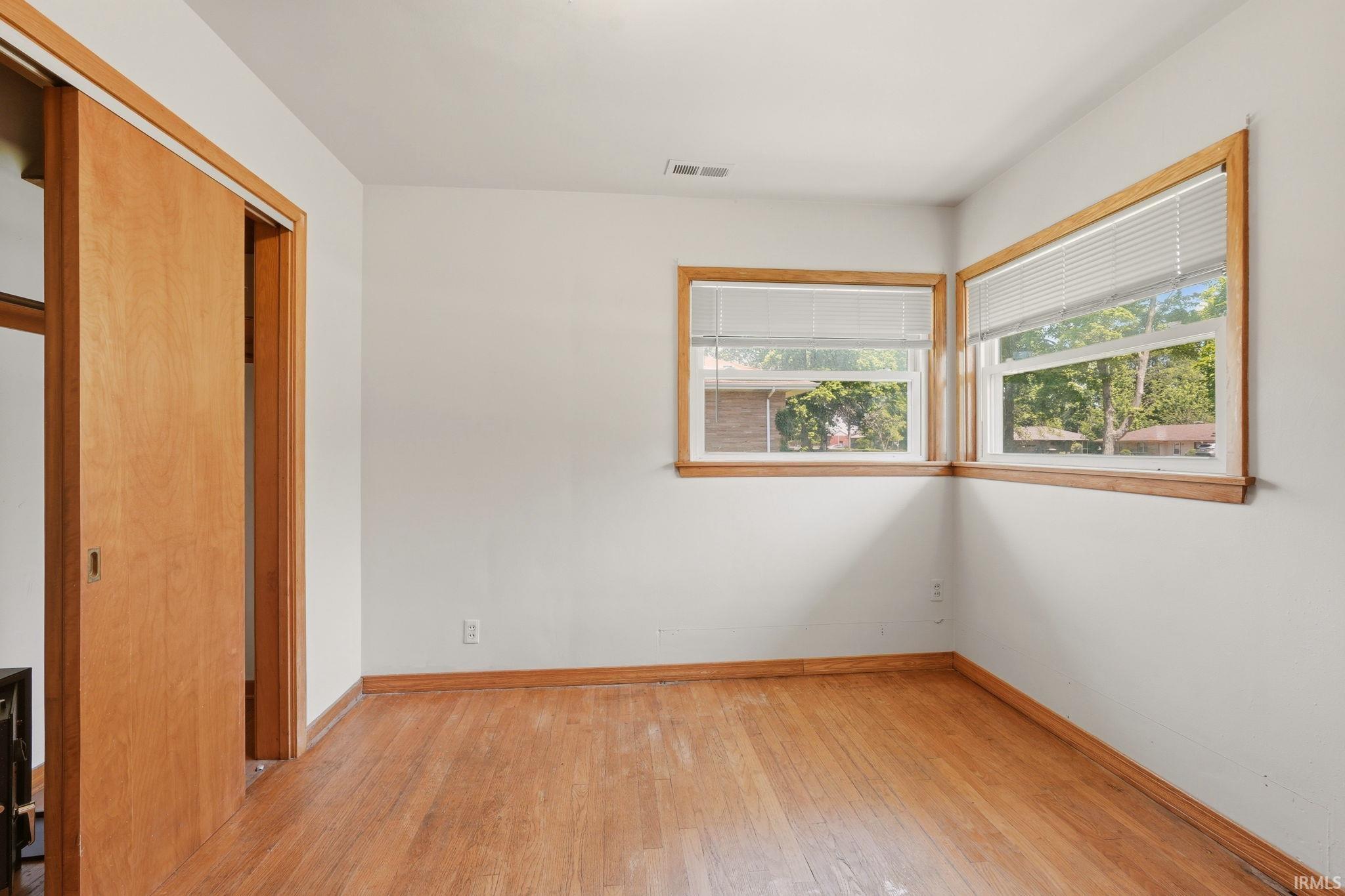 Room featuring wood-finish flooring, two windows with wood trim, and a built-in sliding closet