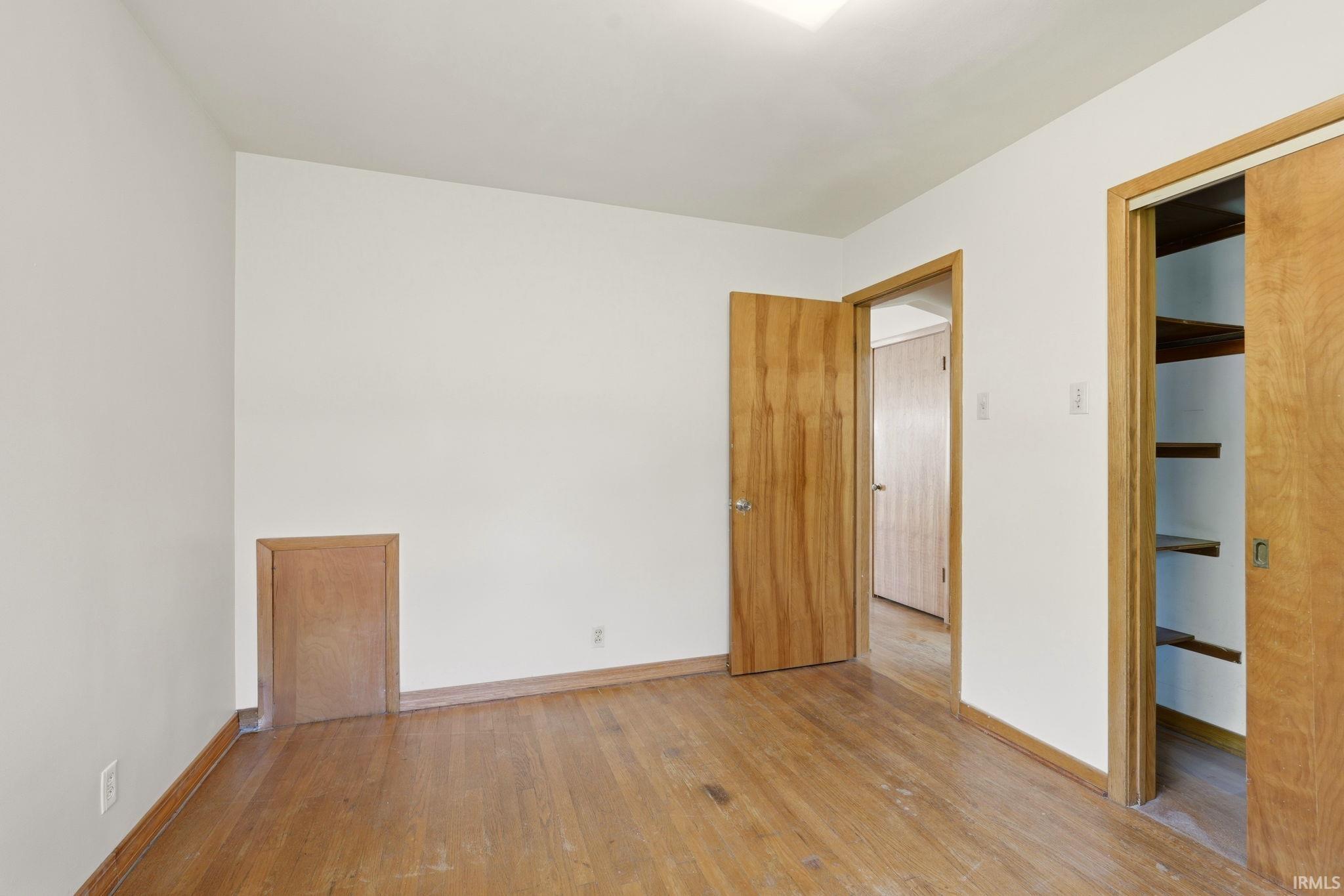 Room featuring wood-finish flooring, light wood doors, and a built-in closet with shelving