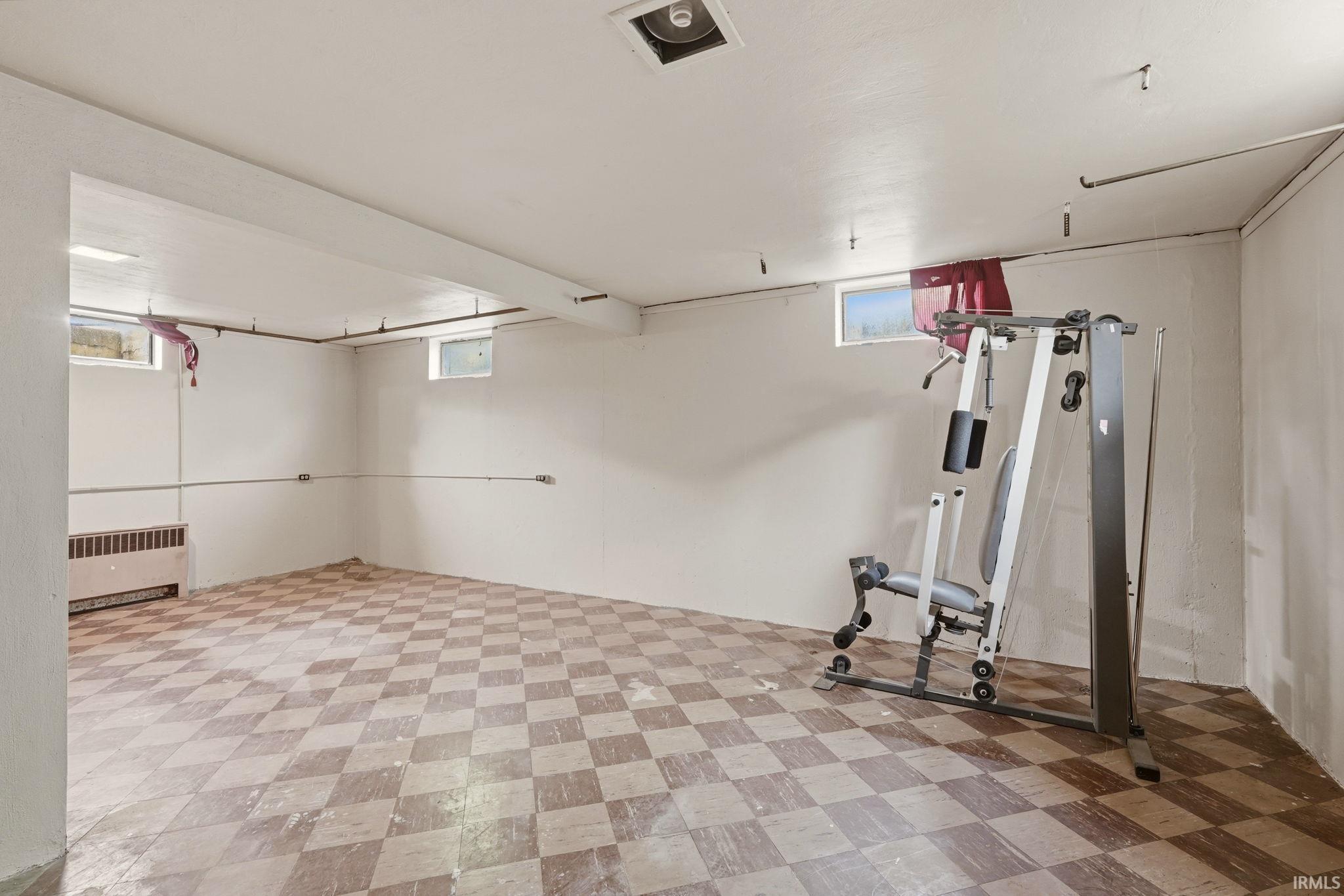 Finished basement space featuring checkerboard tile flooring, white painted walls, and exposed ceiling joists