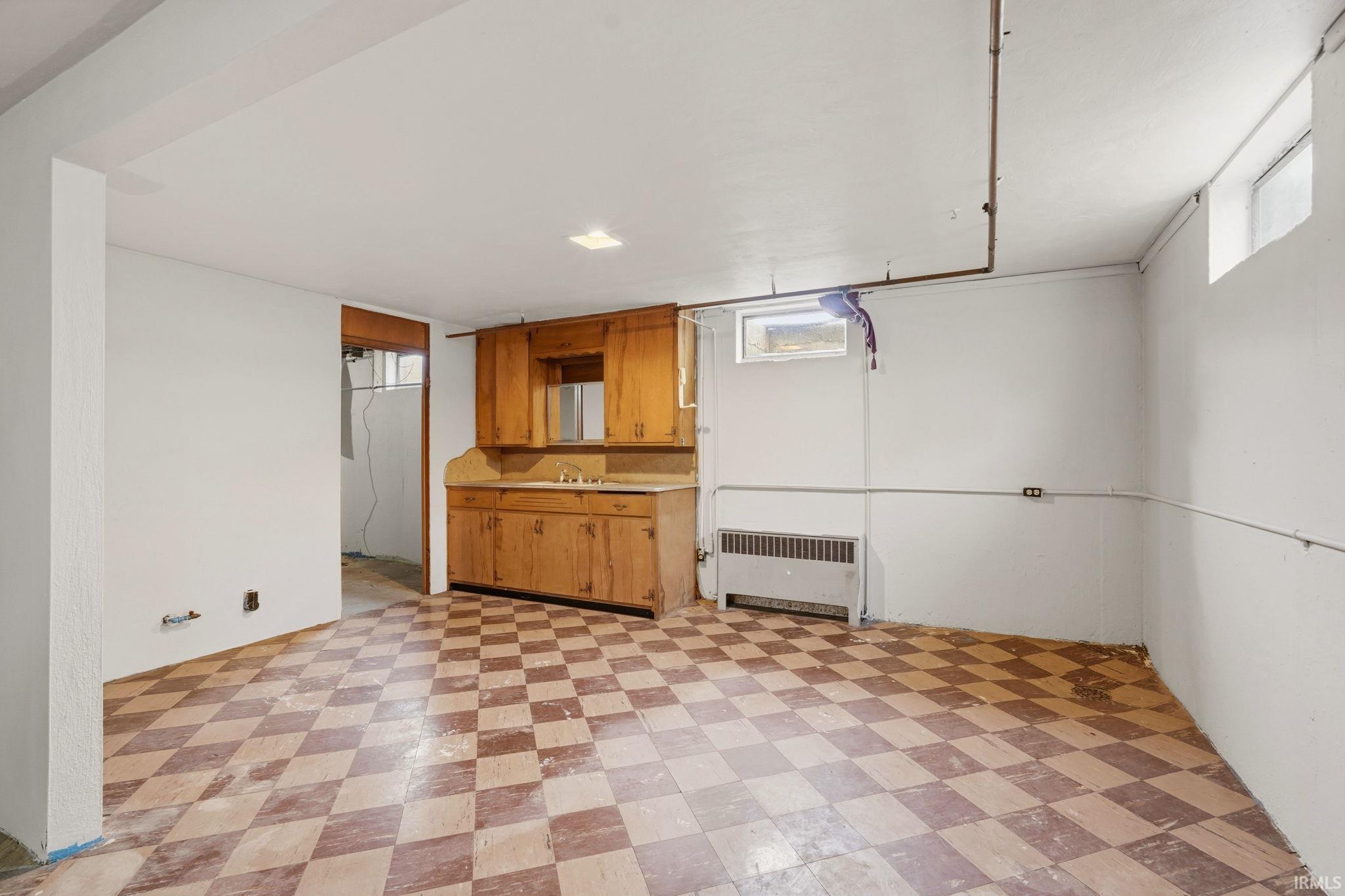 Lower-level room featuring checkerboard-patterned flooring, built-in wooden cabinetry with a sink, and a wall-mounted heating unit