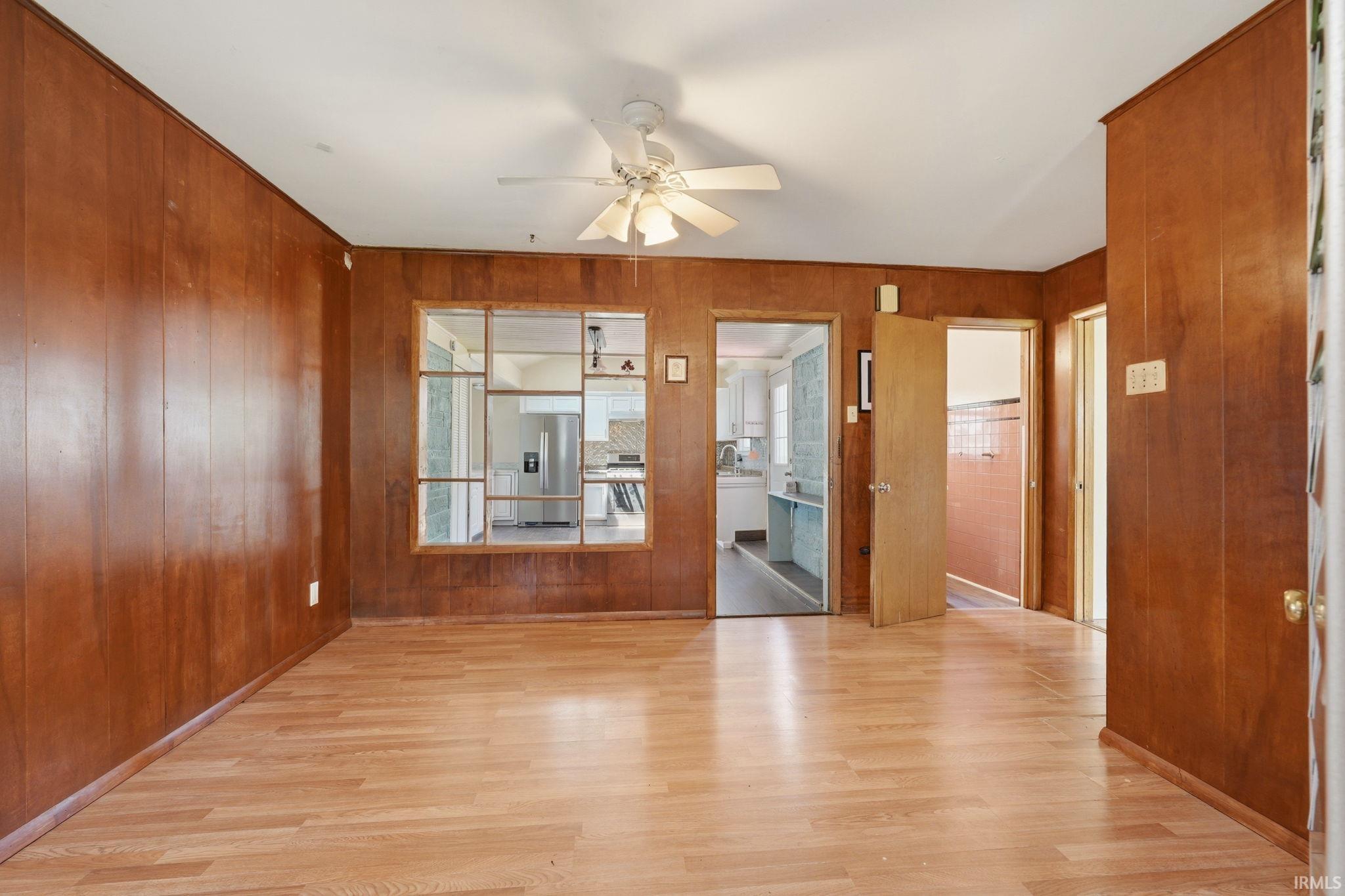 Room featuring wood-finish flooring, wood paneling, and a ceiling fan with light fixture
