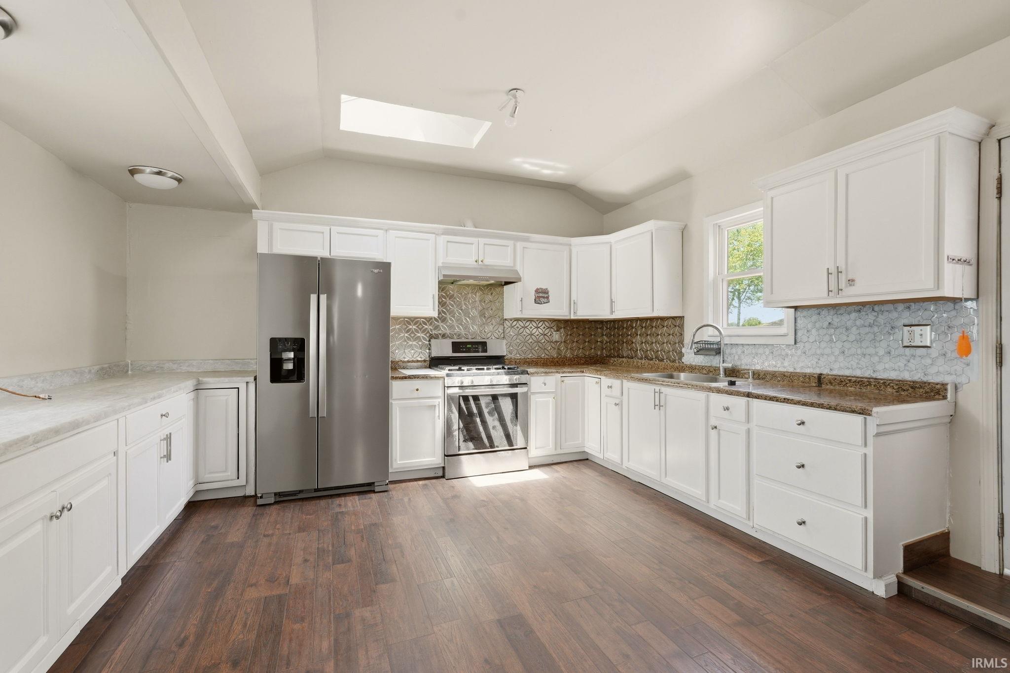 Contemporary kitchen featuring white cabinetry, stainless steel appliances, wood-finish flooring, a skylight, and granite countertops