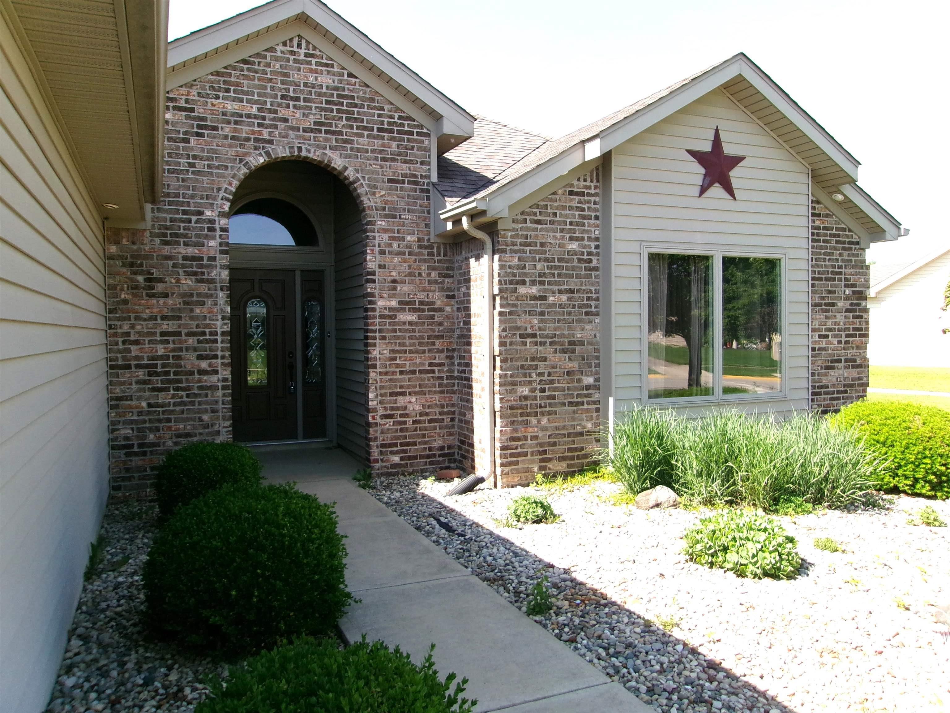 Brick and siding exterior featuring an arched entryway with a decorative glass door, a window with a gabled accent, a concrete walkway, and landscaping with decorative rock and shrubs