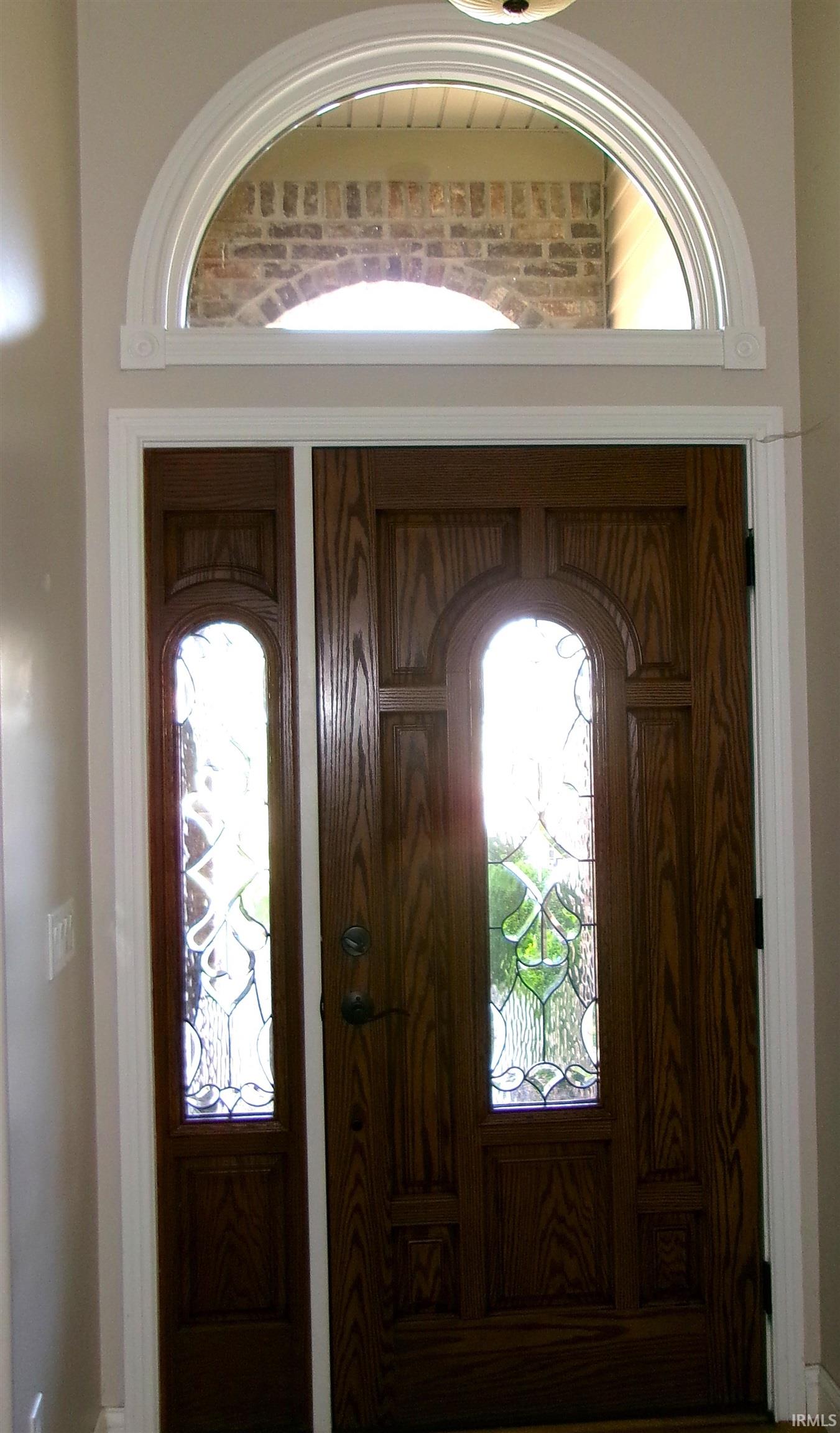 Rich wood-finish entry door with decorative glass inserts and an arched transom window