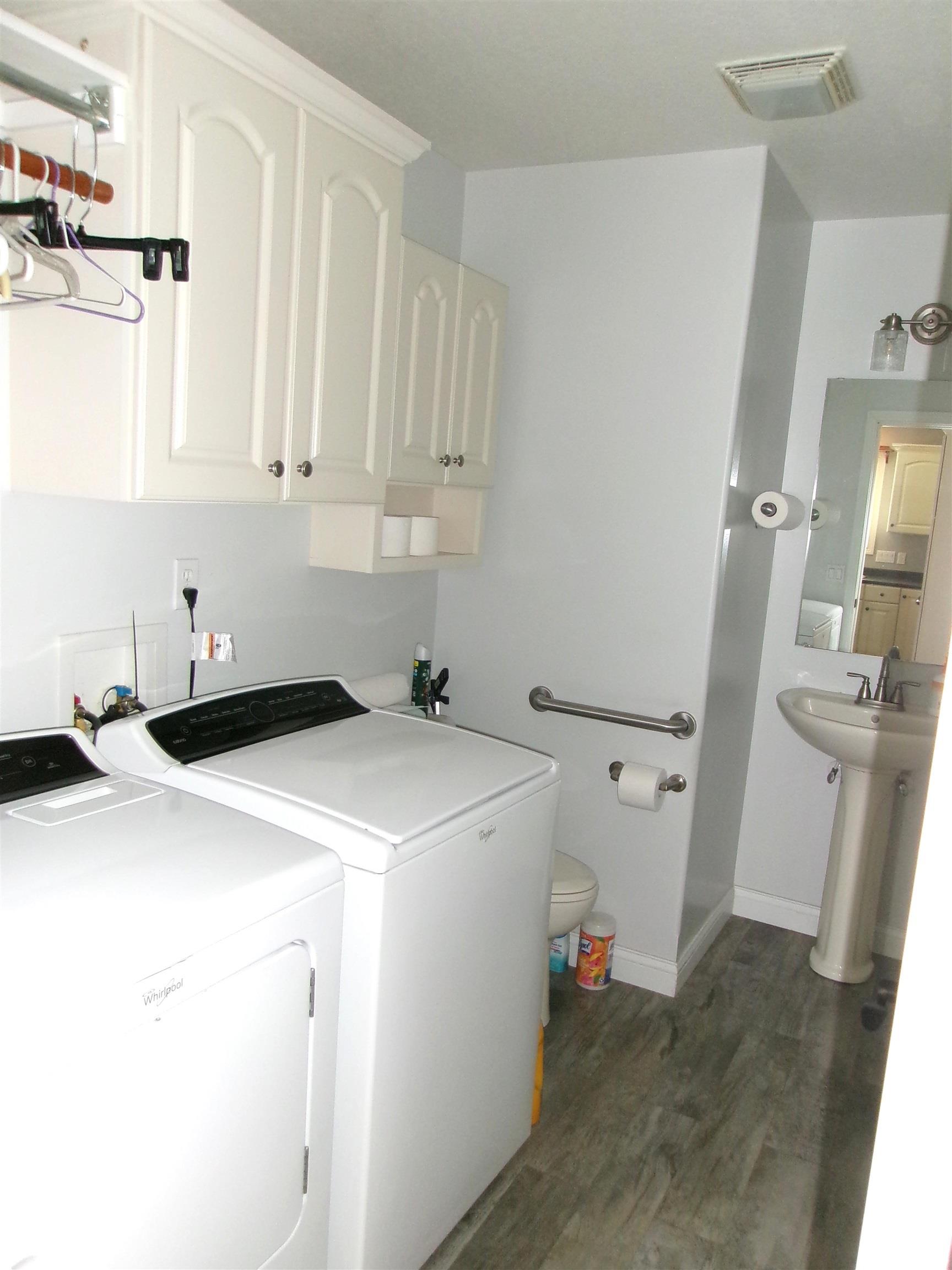 Dedicated laundry area featuring overhead cabinetry, a built-in hanging rod, and wood-finish flooring