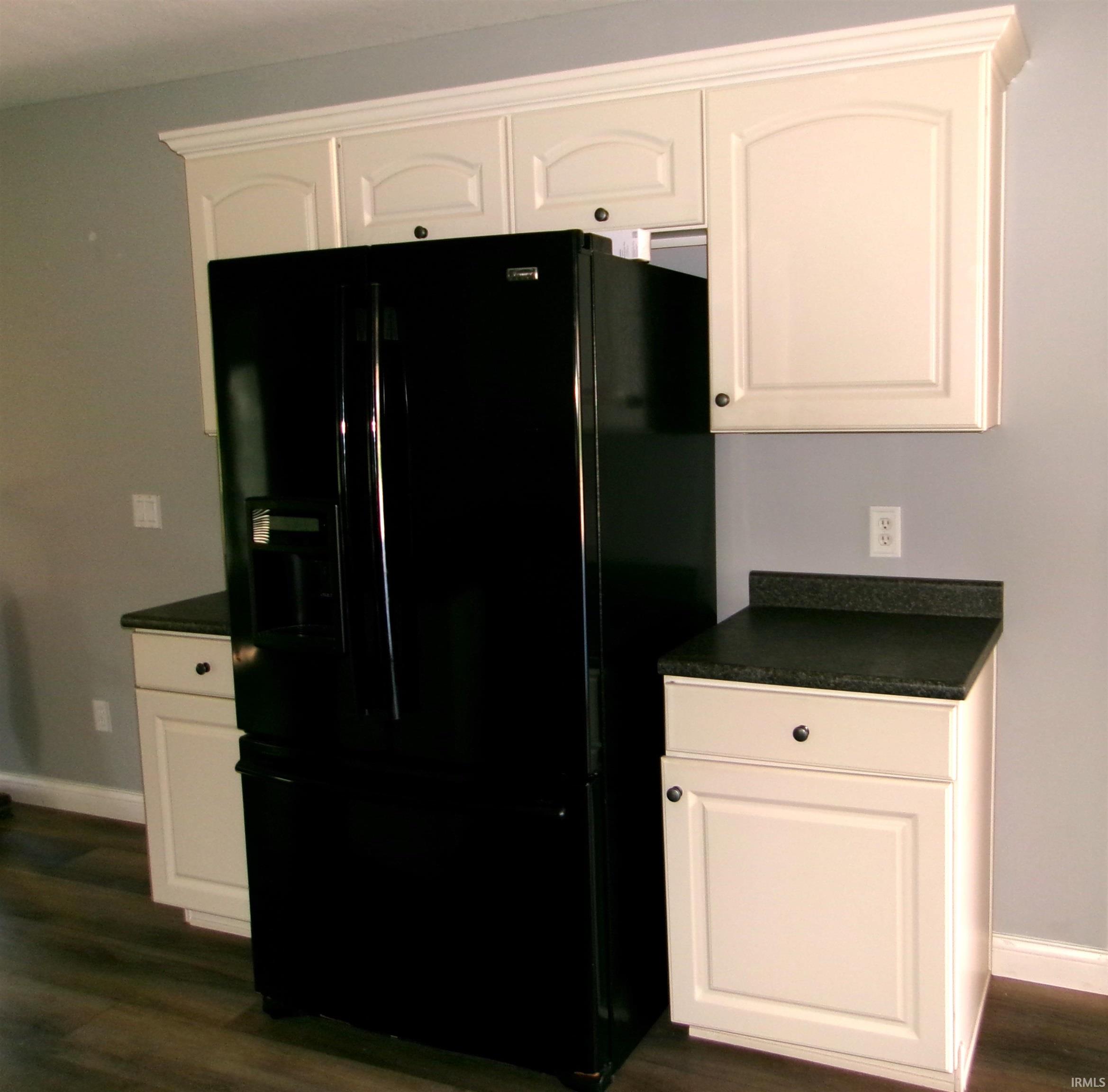 Kitchen area featuring cream-colored upper and lower cabinetry with black hardware, dark speckled countertops, and wood-finish flooring