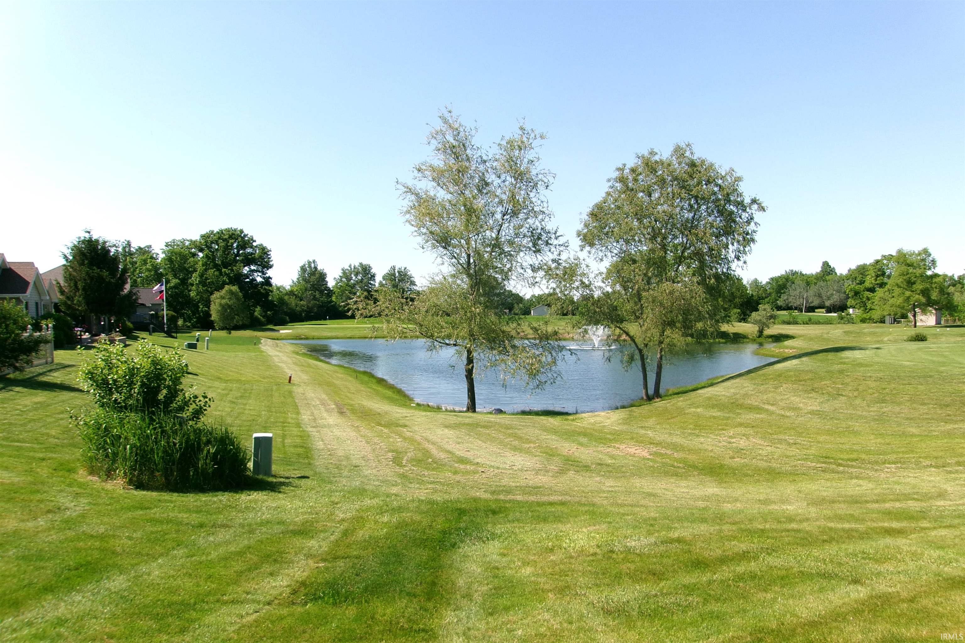 Expansive rear grounds featuring a tranquil pond with a decorative fountain, mature trees, and a substantial lawn