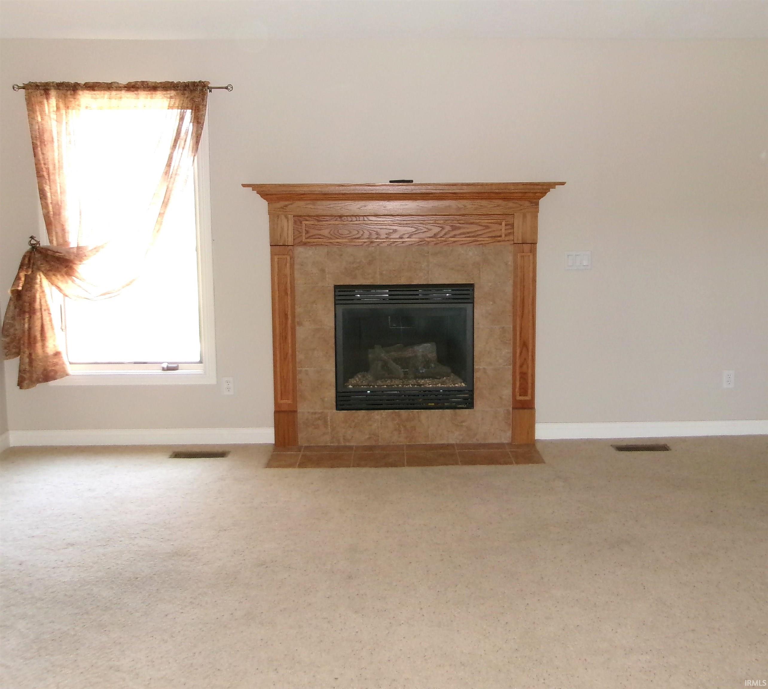 Built-in fireplace featuring a tile surround and a wood mantelpiece, complemented by light-toned wall paint and carpeting