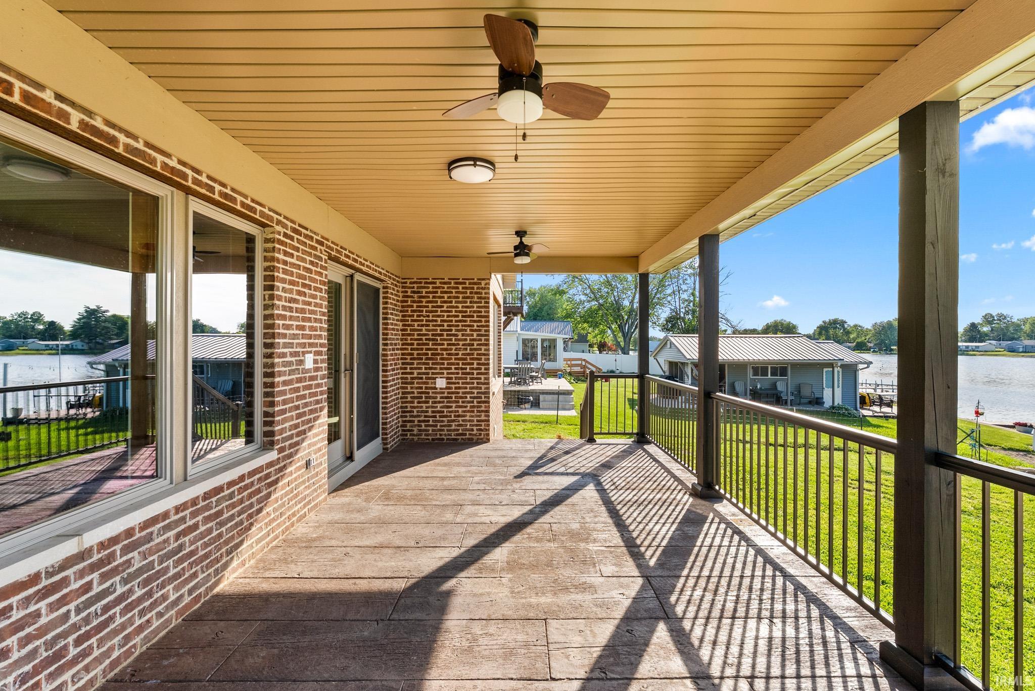 Covered outdoor patio featuring stamped concrete flooring, brick exterior, ceiling fans, and a metal railing system