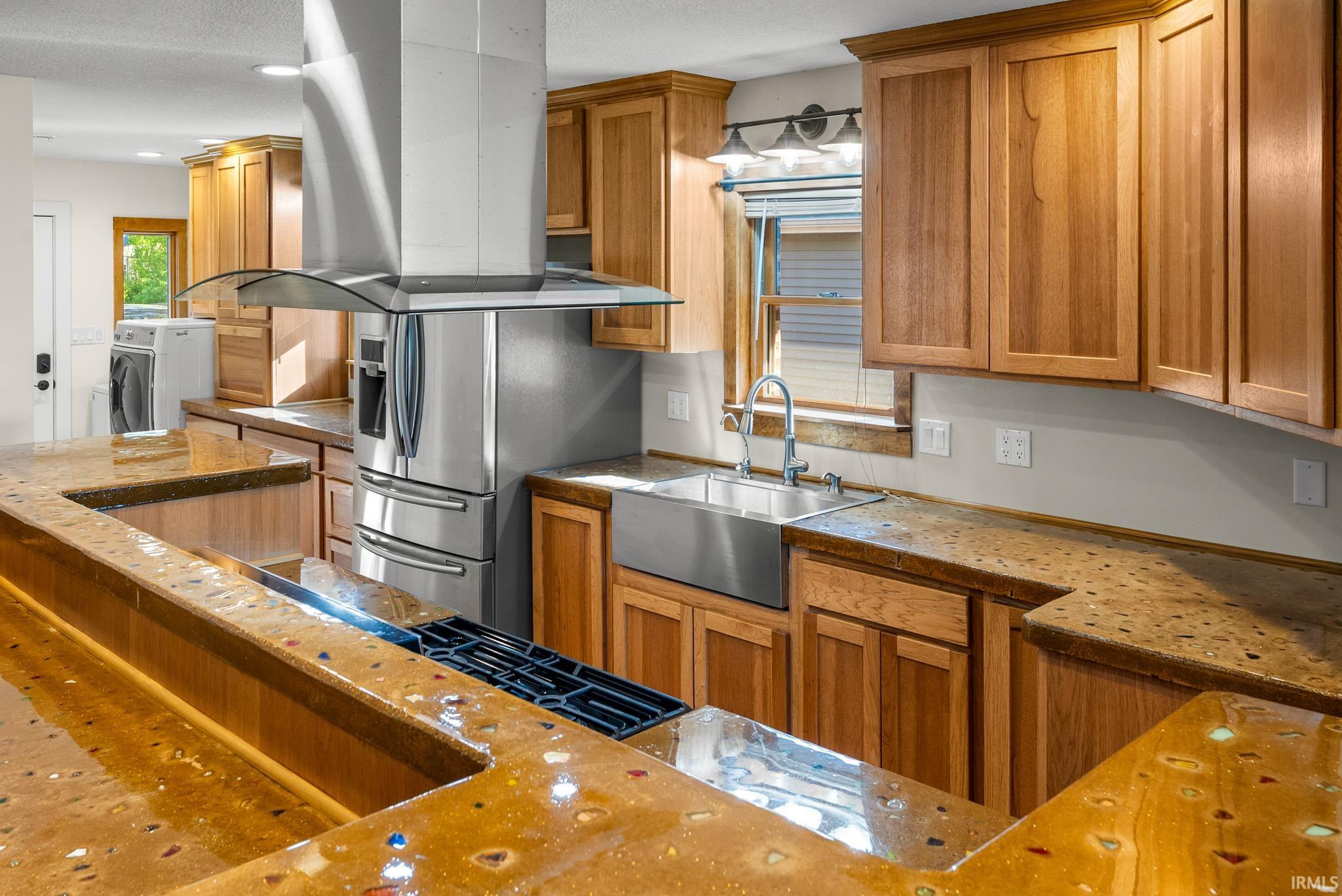 Kitchen featuring custom wood cabinetry with ample storage, a large stainless steel farmhouse sink, and unique epoxy countertops