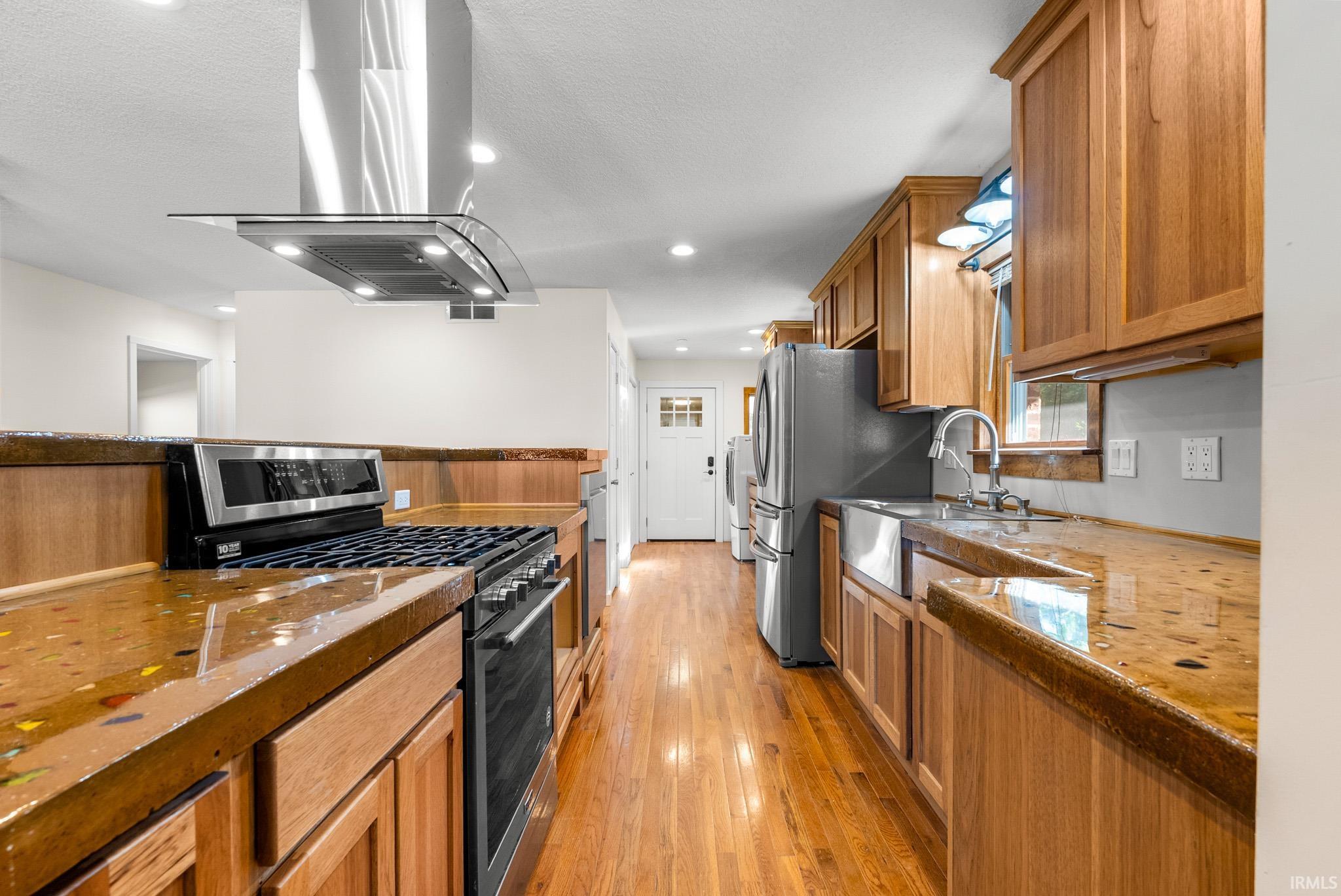 Kitchen featuring wood-finish flooring, stainless steel appliances, a farmhouse sink, and light wood cabinetry