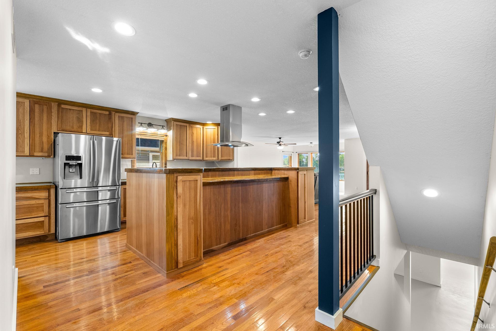 Open-concept kitchen featuring wood-finish flooring, recessed lighting, stainless steel appliances, a center island with a breakfast bar, and wood cabinetry