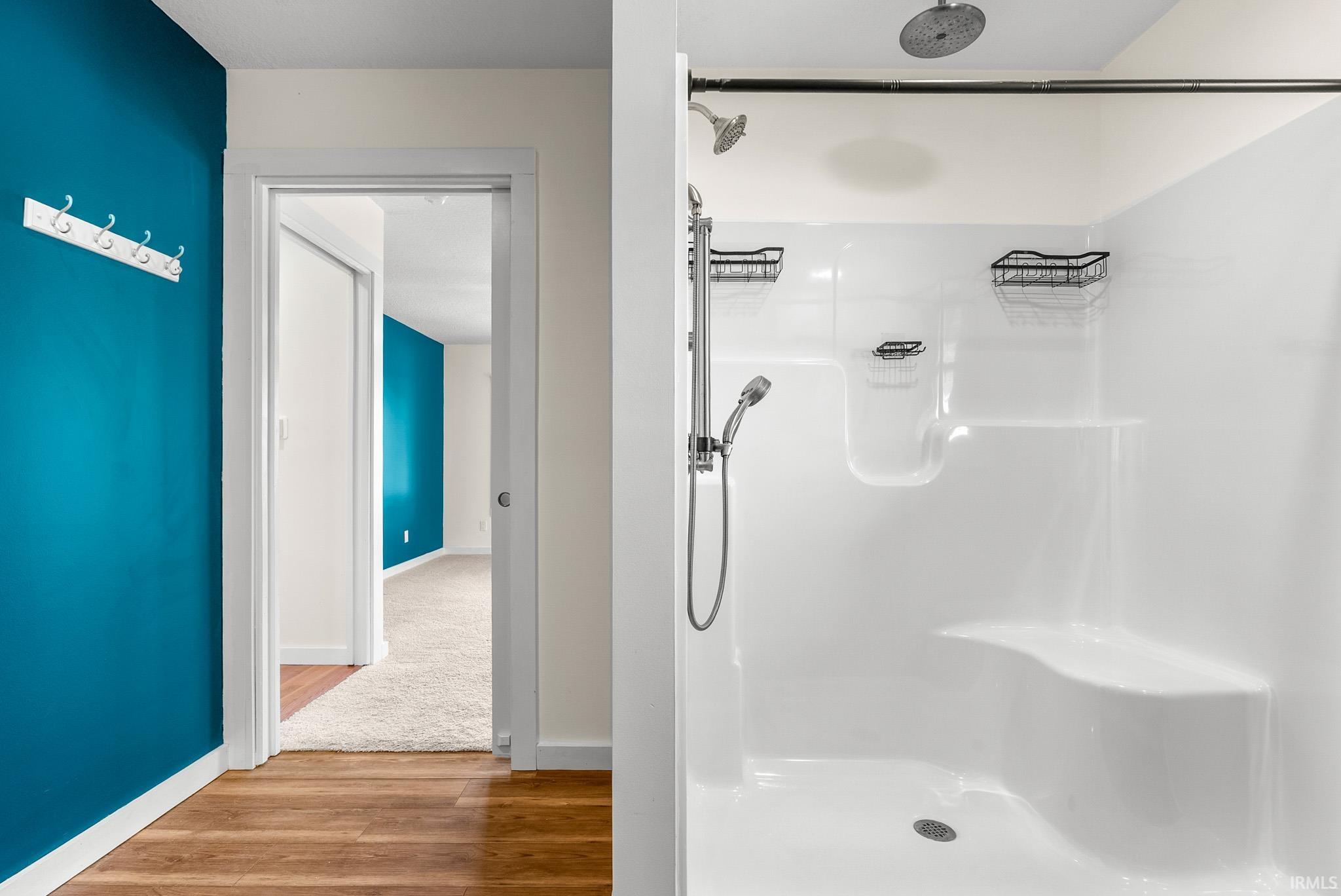 White shower stall featuring a built-in bench, rainfall showerhead, and handheld shower sprayer