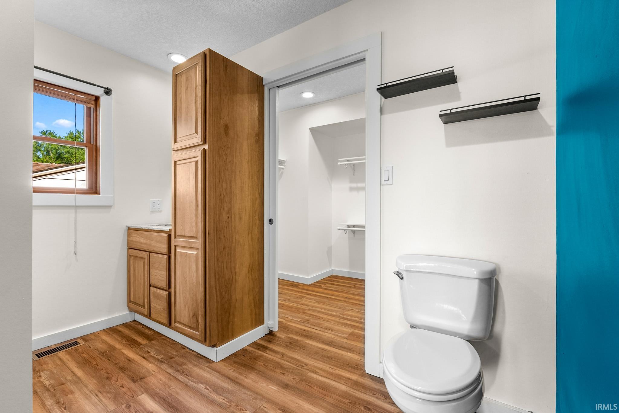 Bathroom featuring wood-finish flooring, a white porcelain toilet, and two wall-mounted shelves