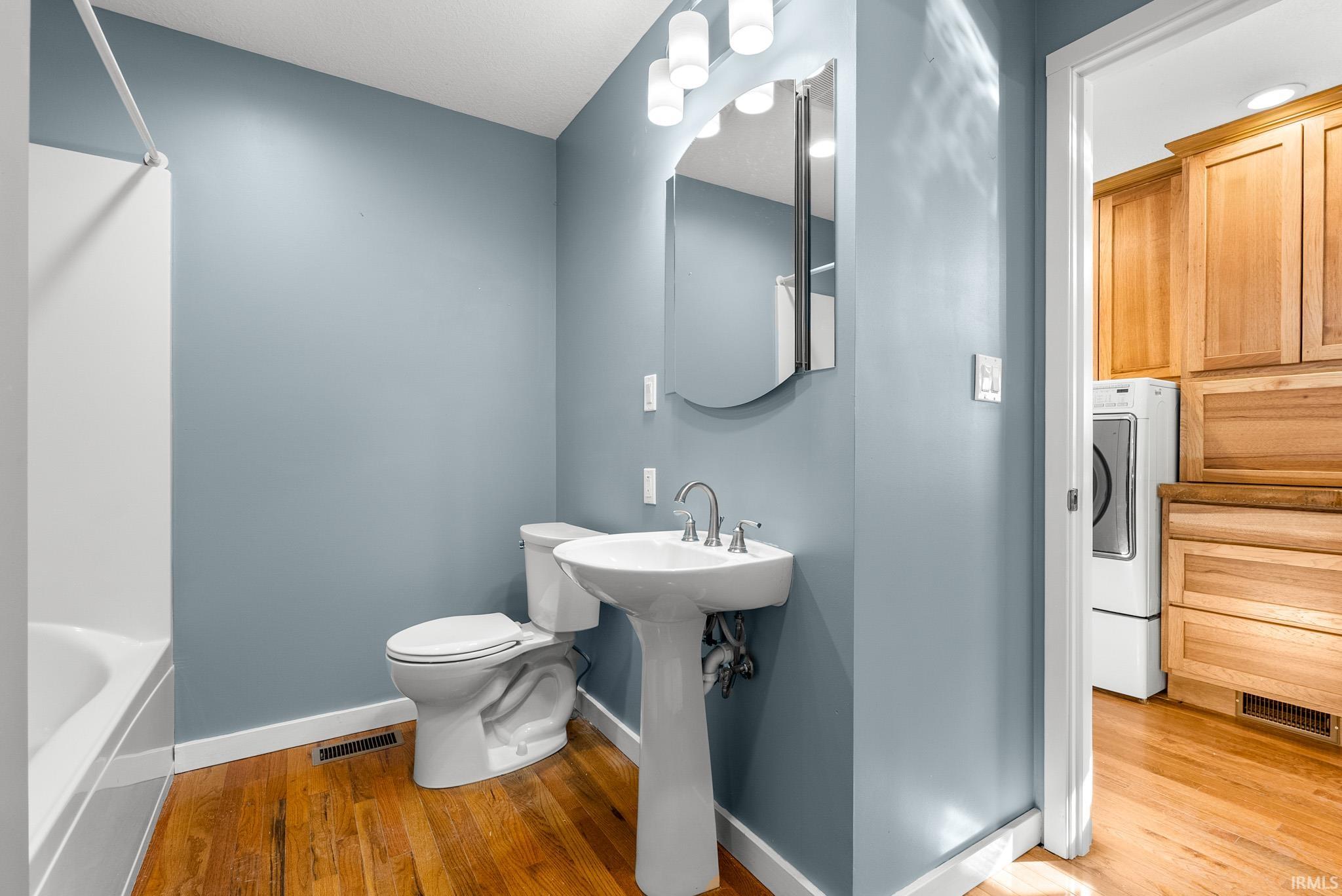 Full bathroom featuring a white pedestal sink, toilet, and bathtub with a shower rod