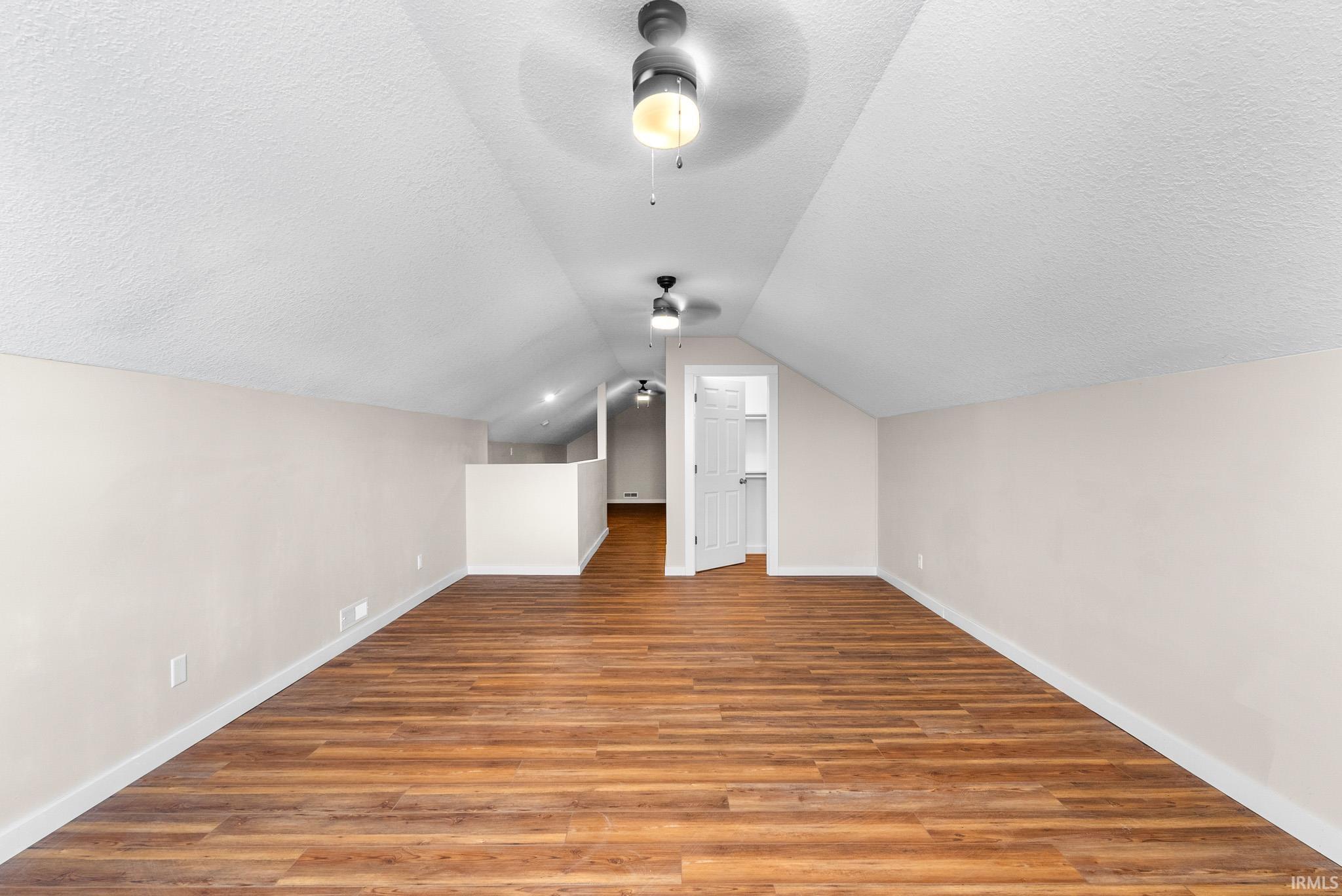 Expansive room featuring wood-finish flooring, neutral-toned walls, and a vaulted ceiling
