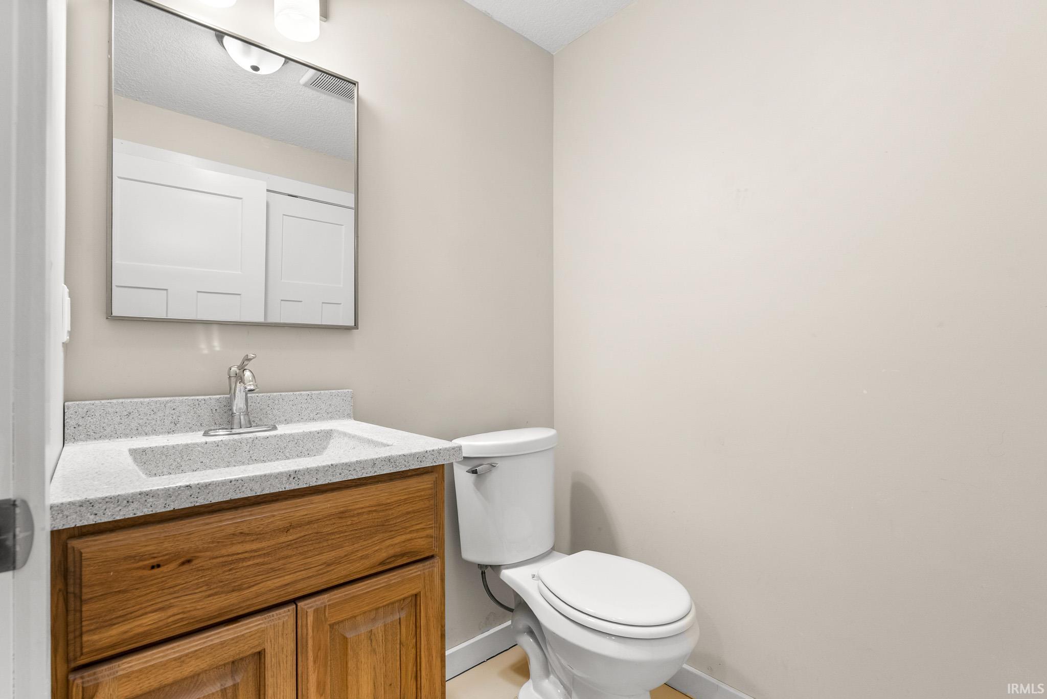 Bathroom featuring a wood-finish vanity with a light speckled countertop, an undermount sink, and a framed wall mirror