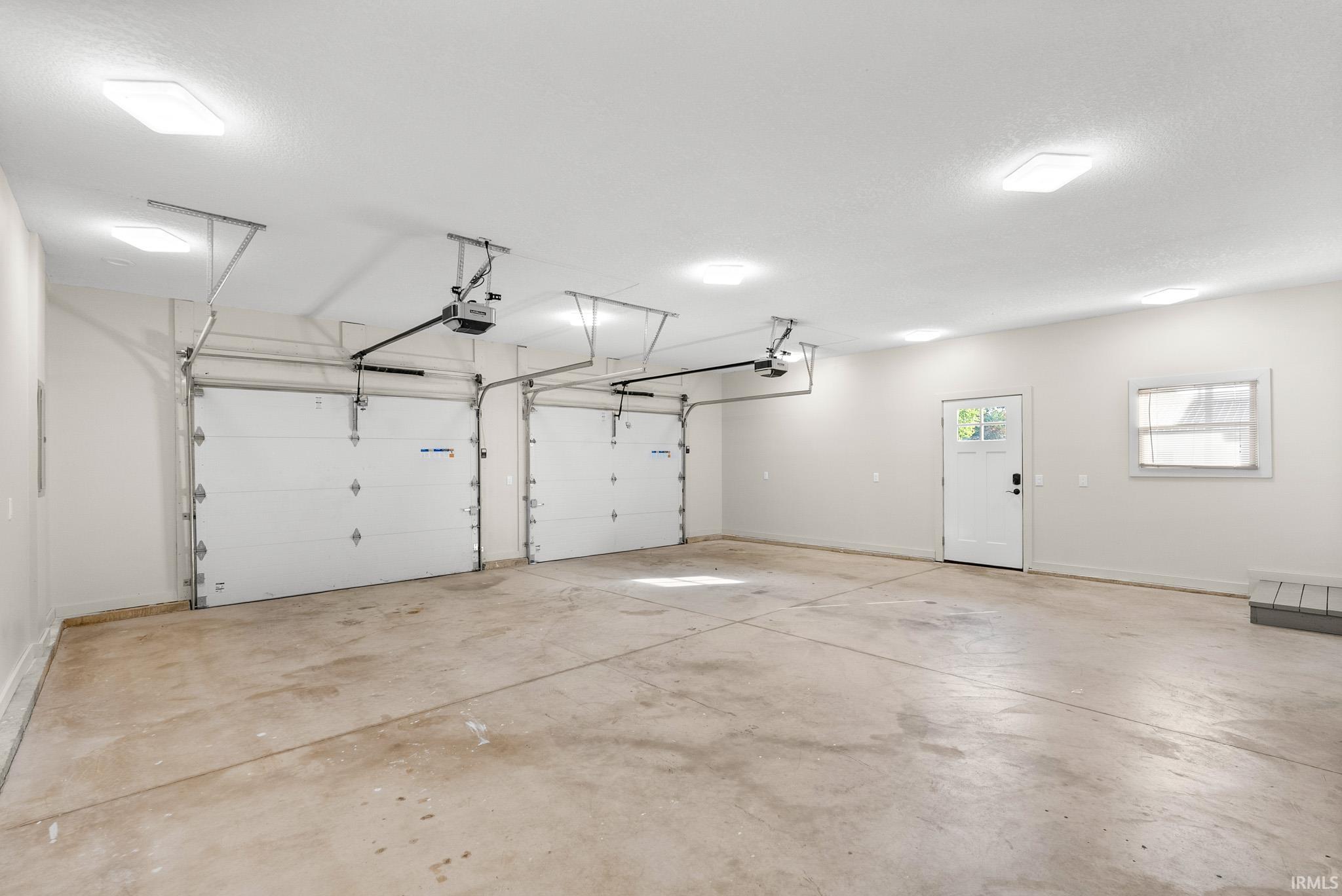 Spacious three-car garage featuring automatic openers, multiple recessed ceiling lights, an exterior side door with glass inserts, and a casement window