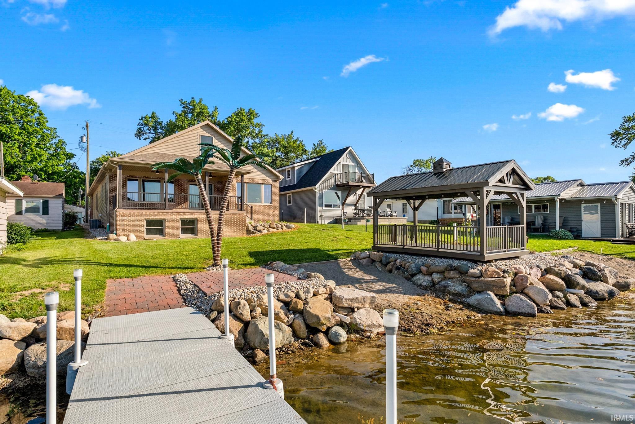 Waterfront property featuring a private dock, a brick paver pathway, and a covered gazebo with a metal roof
