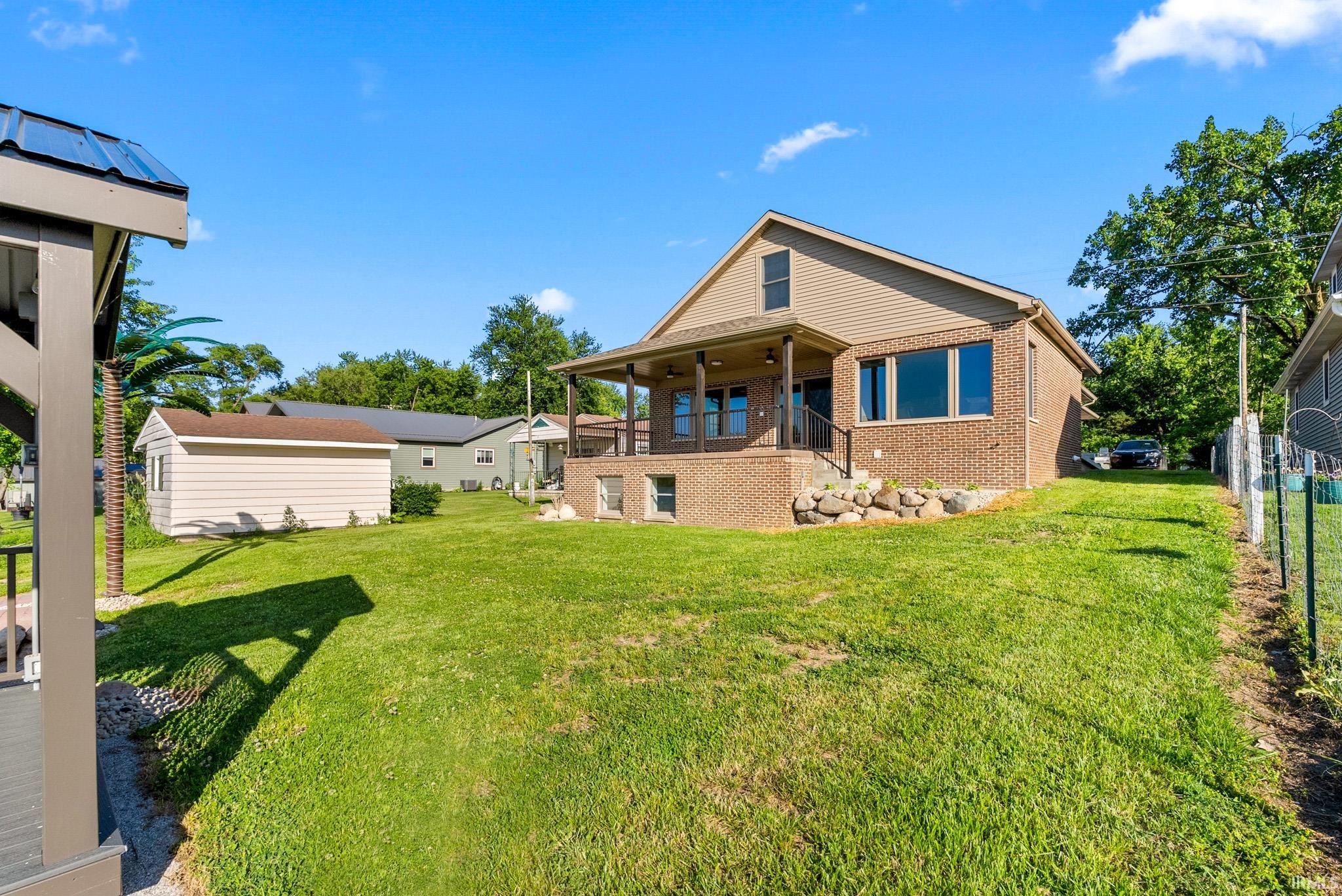Expansive green lawn surrounds a brick and siding residence with a covered front porch, an upper-level window, and a separate storage shed