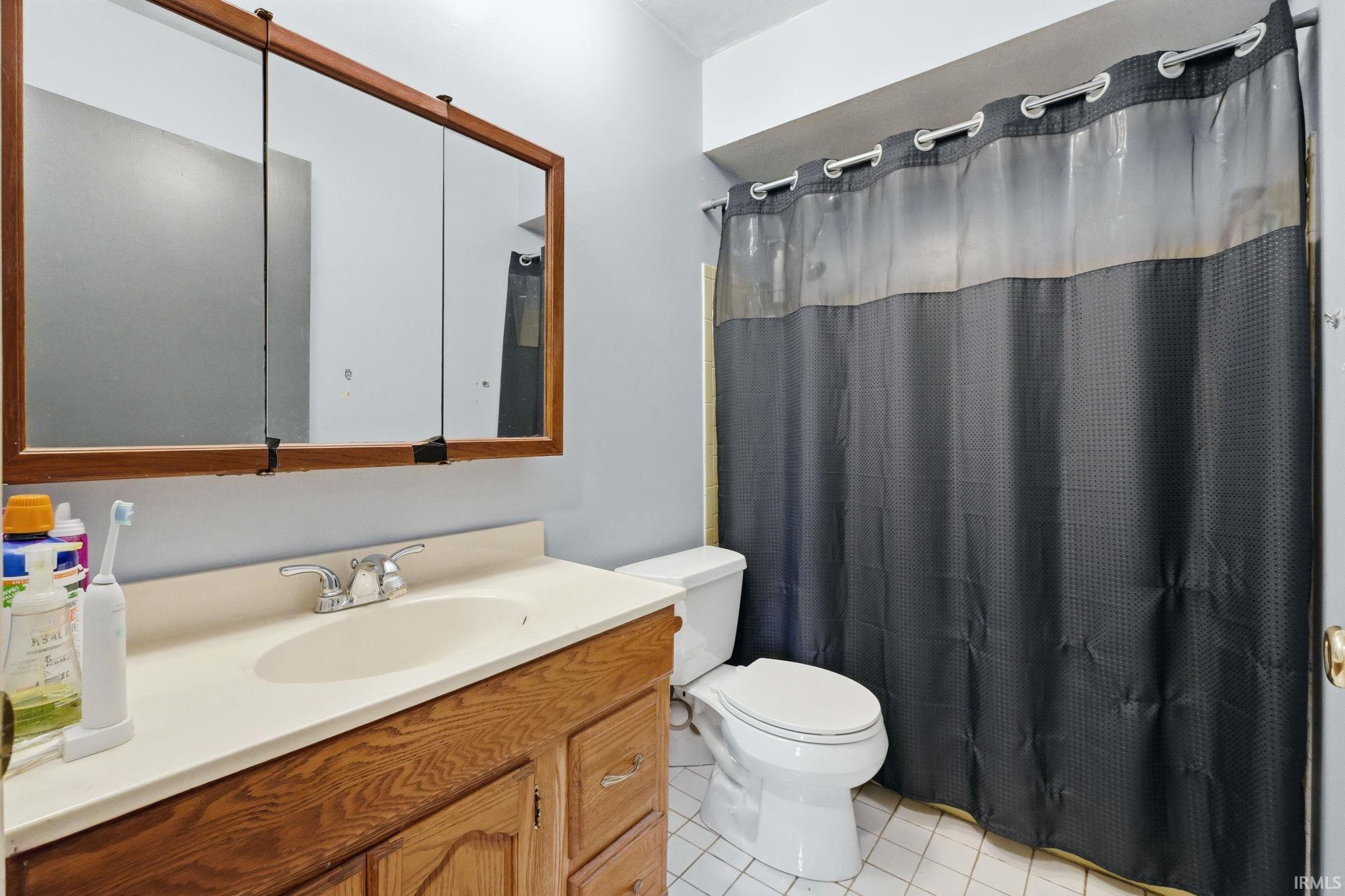 Bathroom featuring a wood-finish vanity with a built-in sink, a wall-mounted medicine cabinet with a wood-finish frame, and white tile flooring