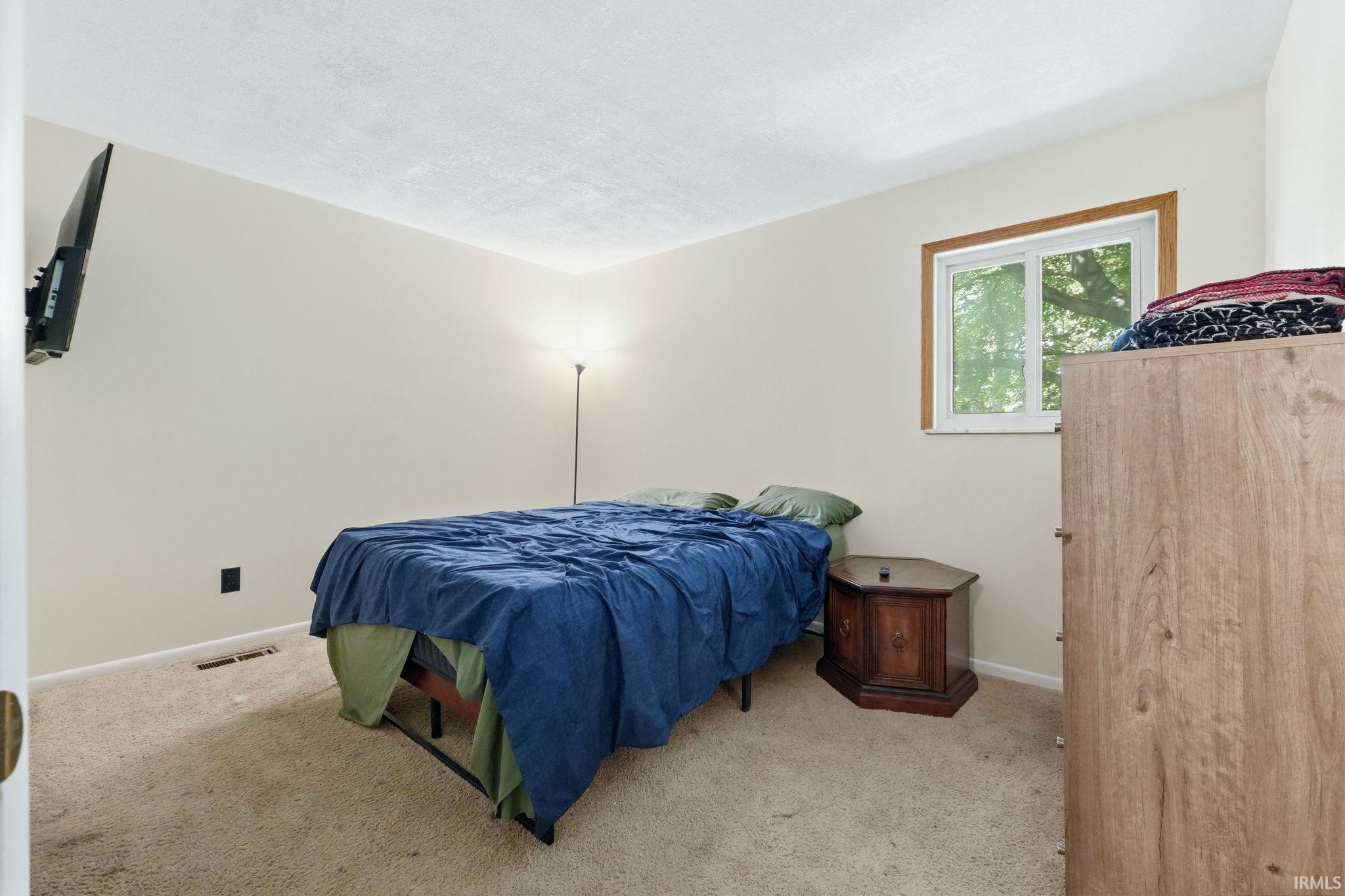 Carpeted room featuring a white-framed window with wood trim, neutral wall paint, and a textured ceiling