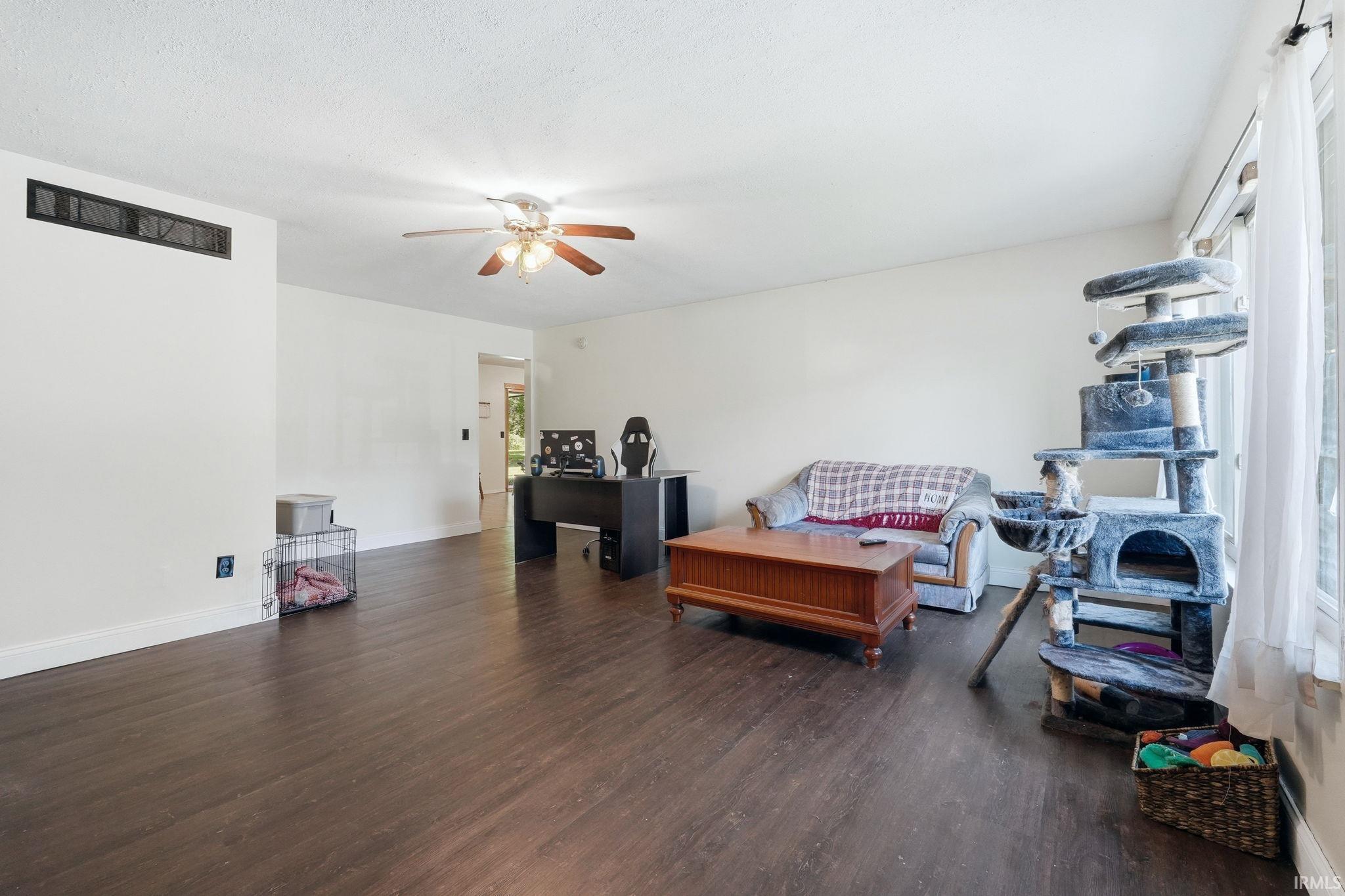 Spacious interior room featuring dark wood-finish flooring, white walls, and a ceiling fan with integrated lighting