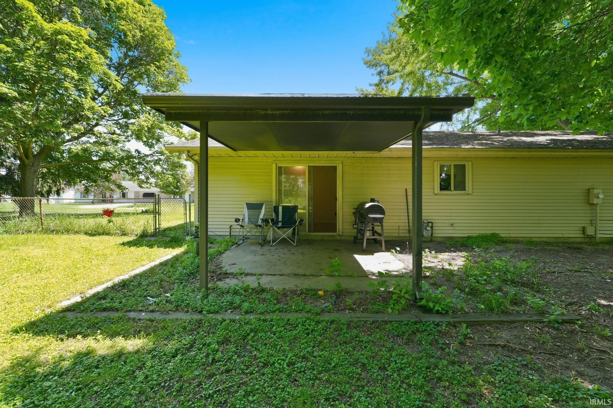 Rear exterior featuring a covered concrete patio, sliding glass door access, an additional window, light-colored siding, and a partial chain-link fence