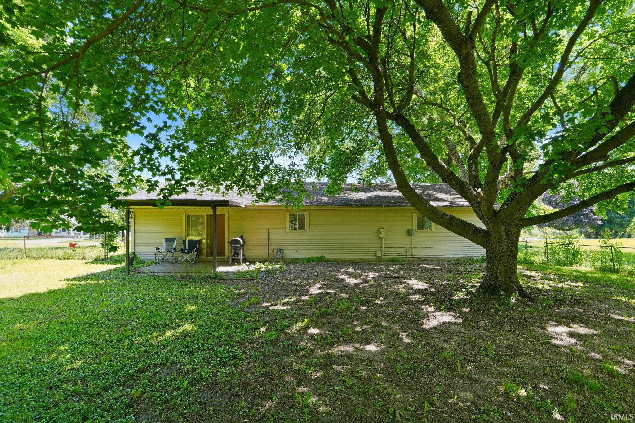 Expansive rear yard featuring a large mature tree, a covered patio area, and a light-colored siding exterior