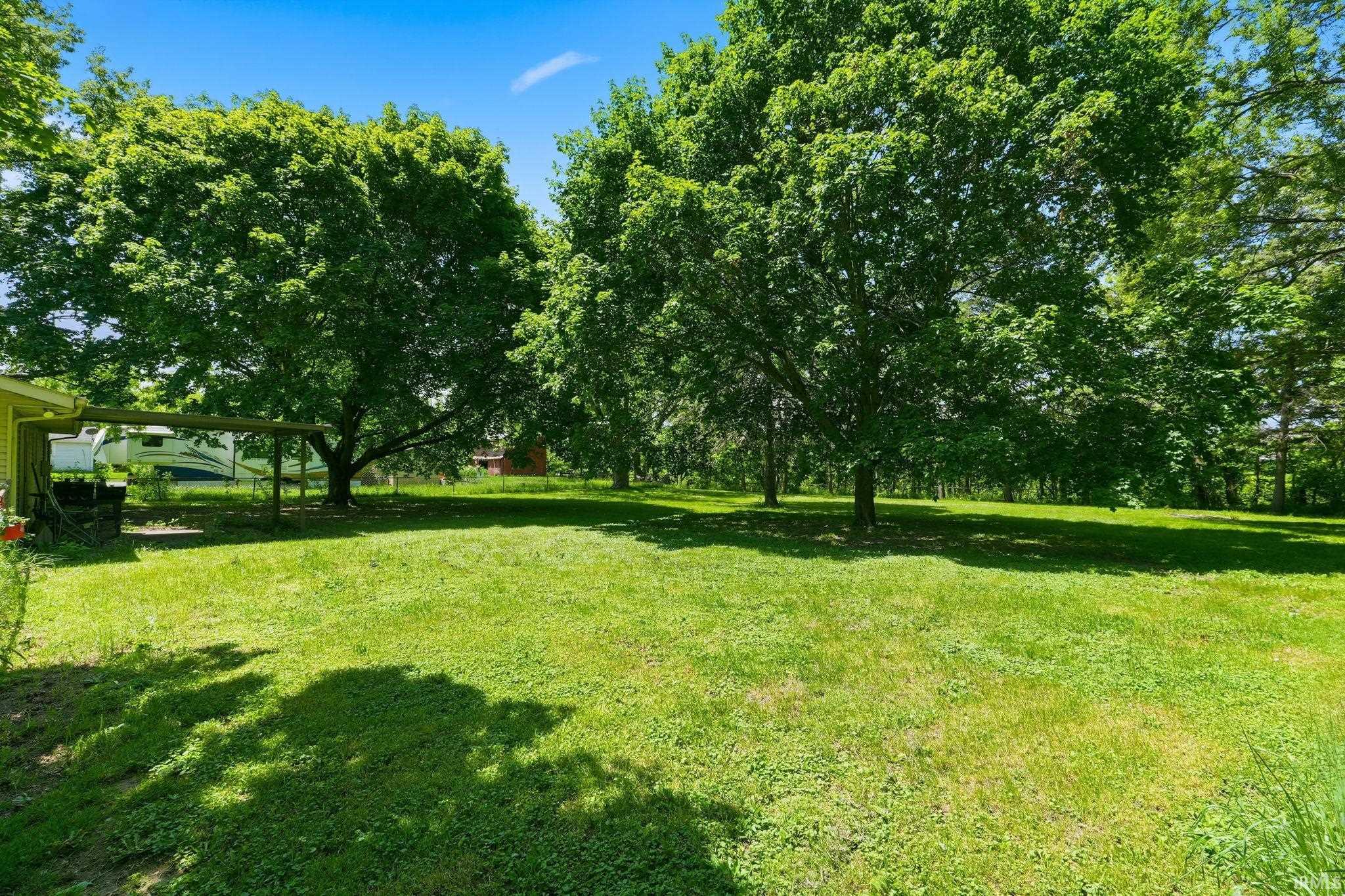 Expansive green lawn with mature shade trees and a partial view of an adjacent structure with a covered awning
