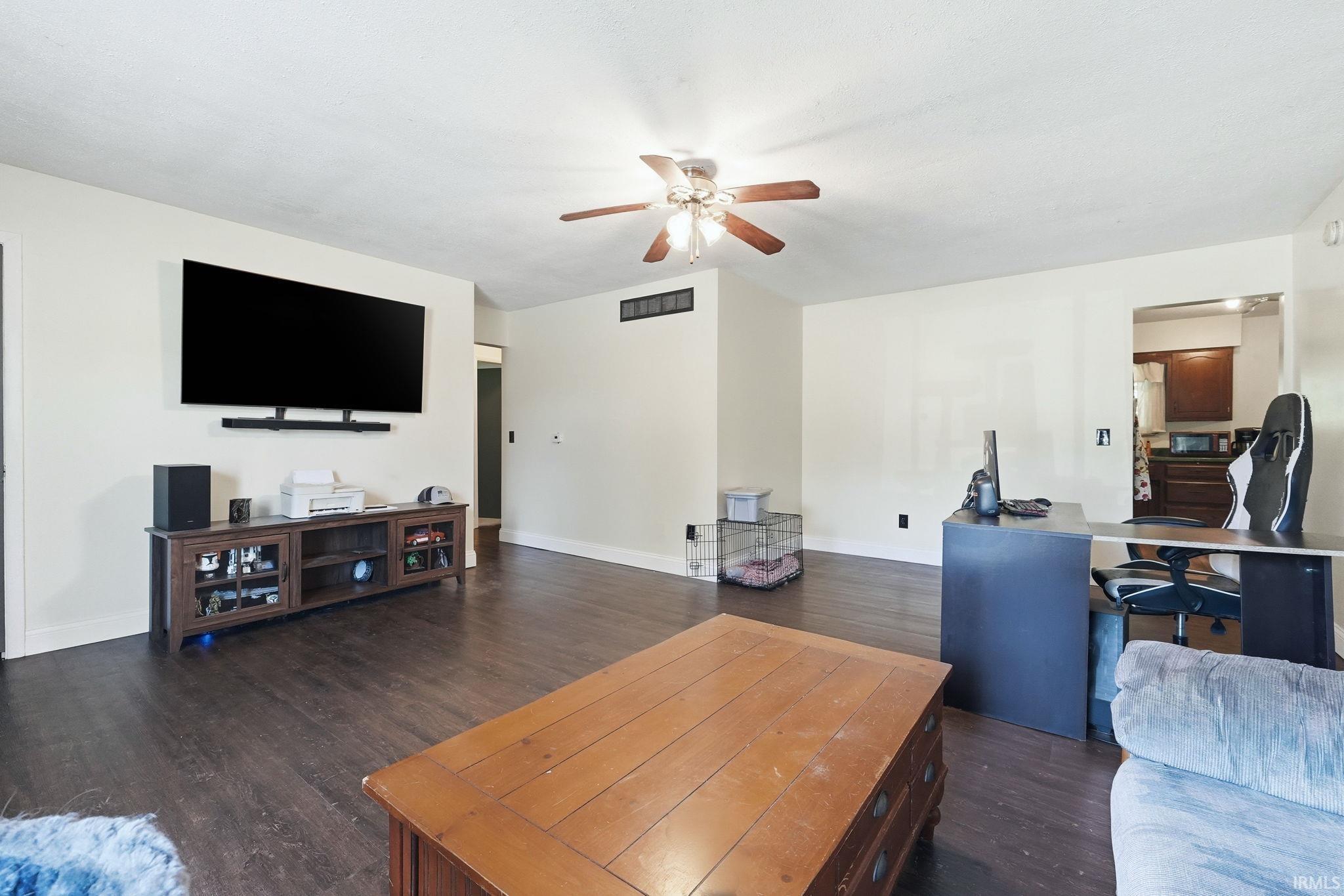 Spacious living area featuring wood-finish flooring, light-colored walls, and a ceiling fan