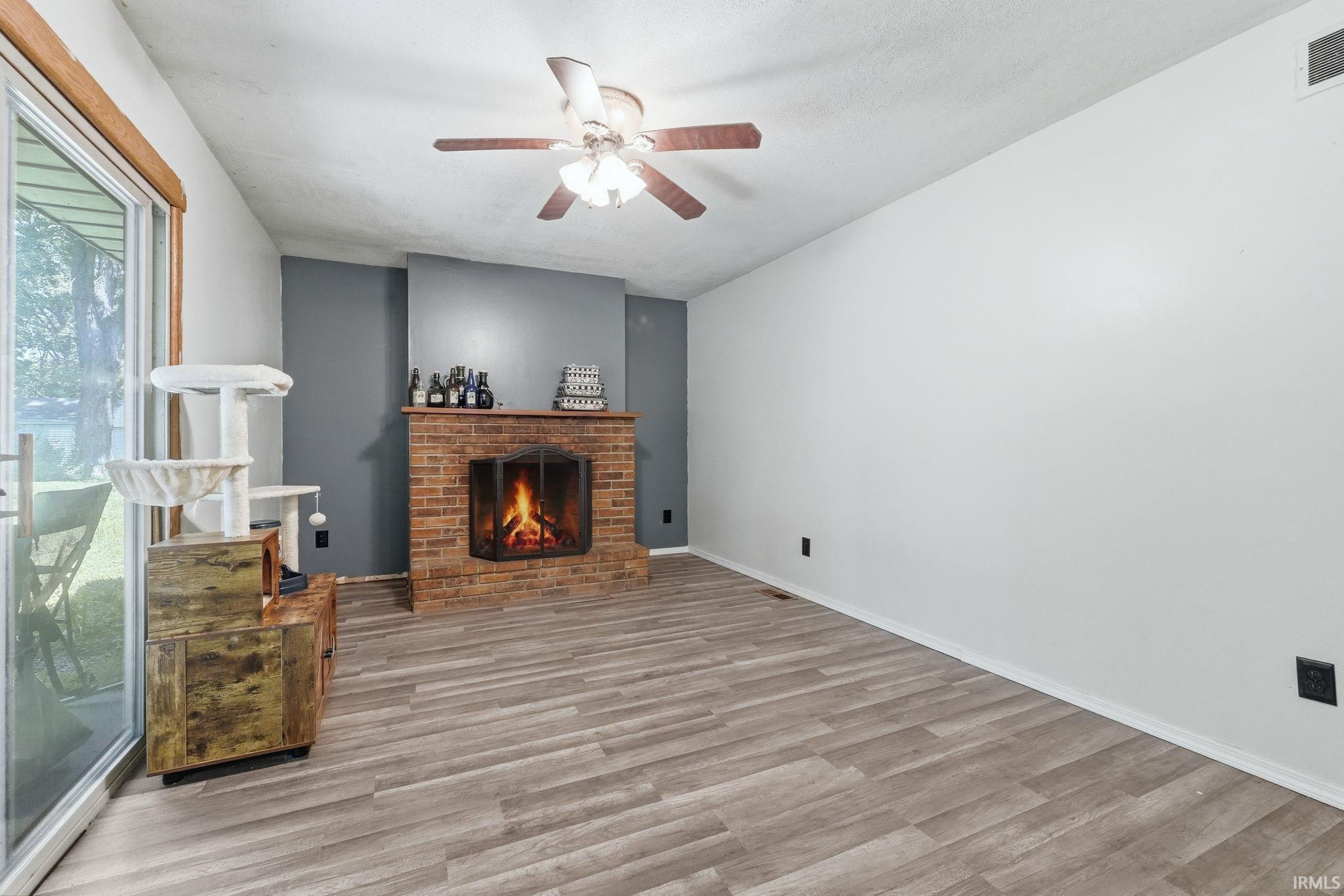 Living area featuring a brick fireplace with a mantel, wood-finish flooring, and a ceiling fan