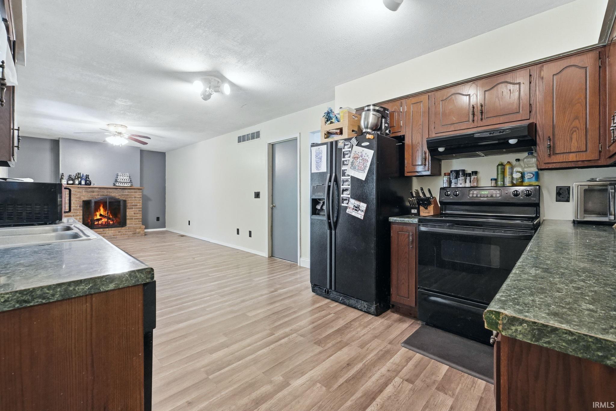 Open-concept kitchen featuring wood-finish flooring, dark-toned cabinetry, and a black appliance suite