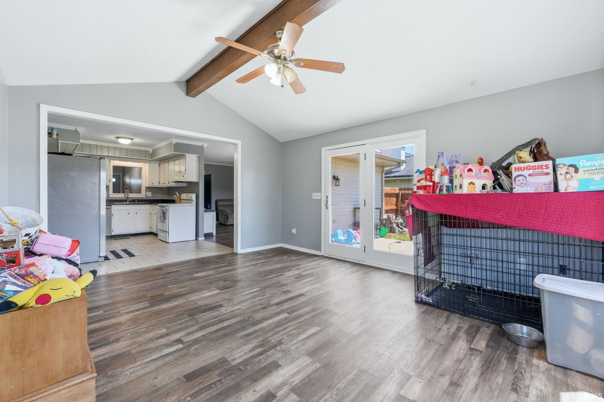 Spacious room featuring vaulted ceilings with exposed wood beams, a ceiling fan, and wood-finish flooring
