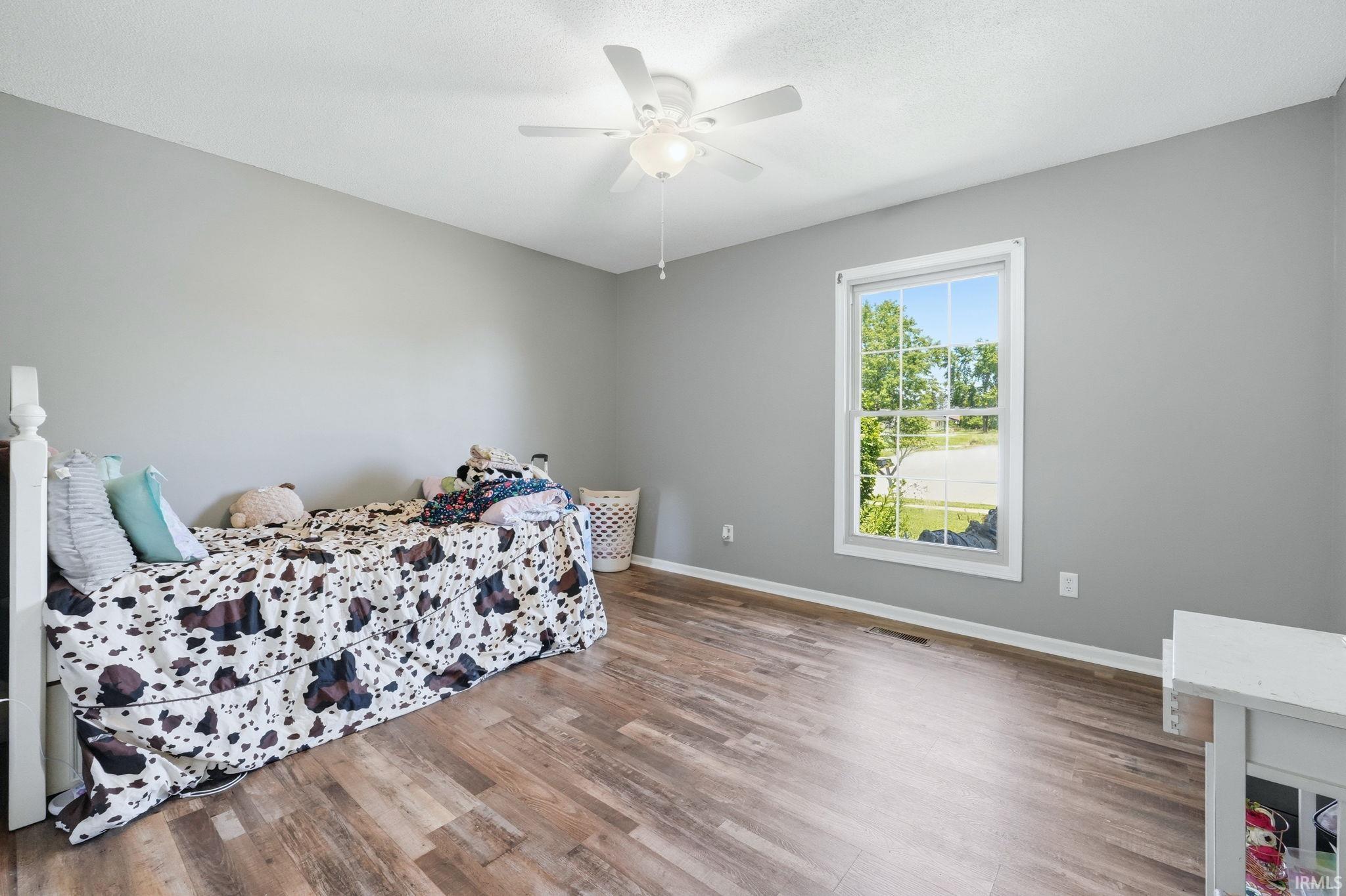 Spacious room featuring wood-finish flooring, a ceiling fan, and a large window providing ample natural light