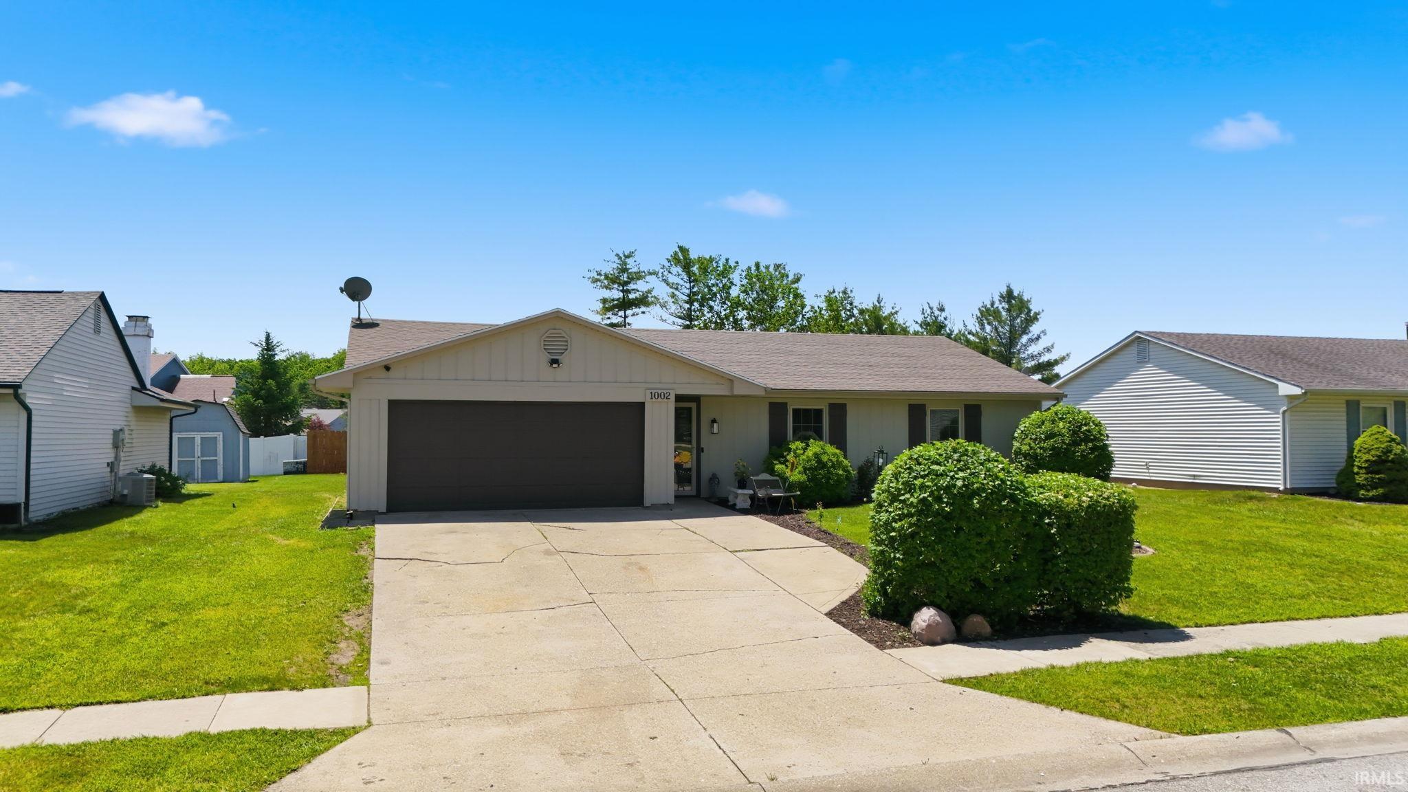 Ranch-style residence featuring a prominent two-car garage, mature landscaping, and a concrete driveway