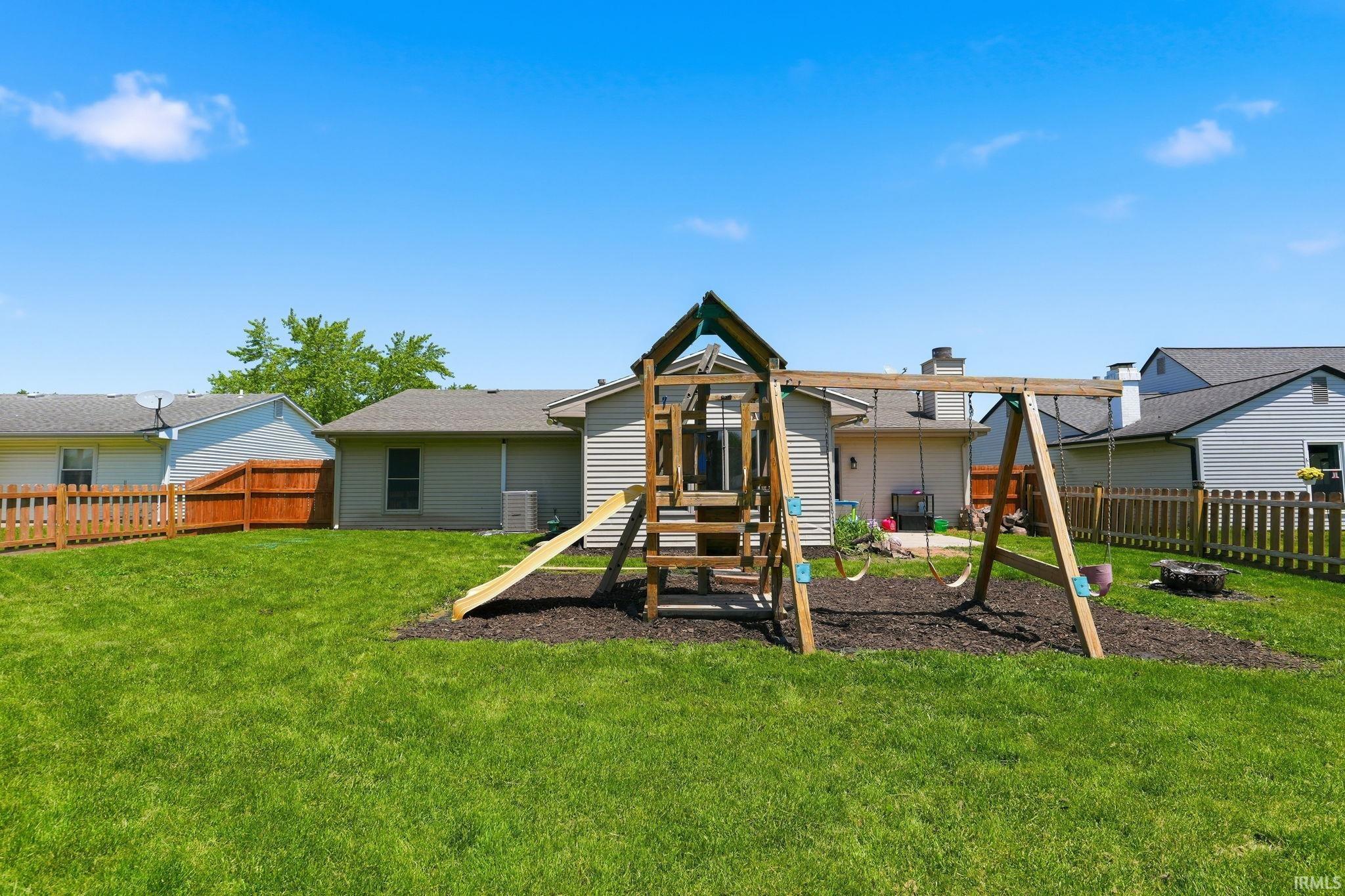 Expansive backyard featuring a manicured lawn, a wooden playset with slide and swings, and partial privacy fencing