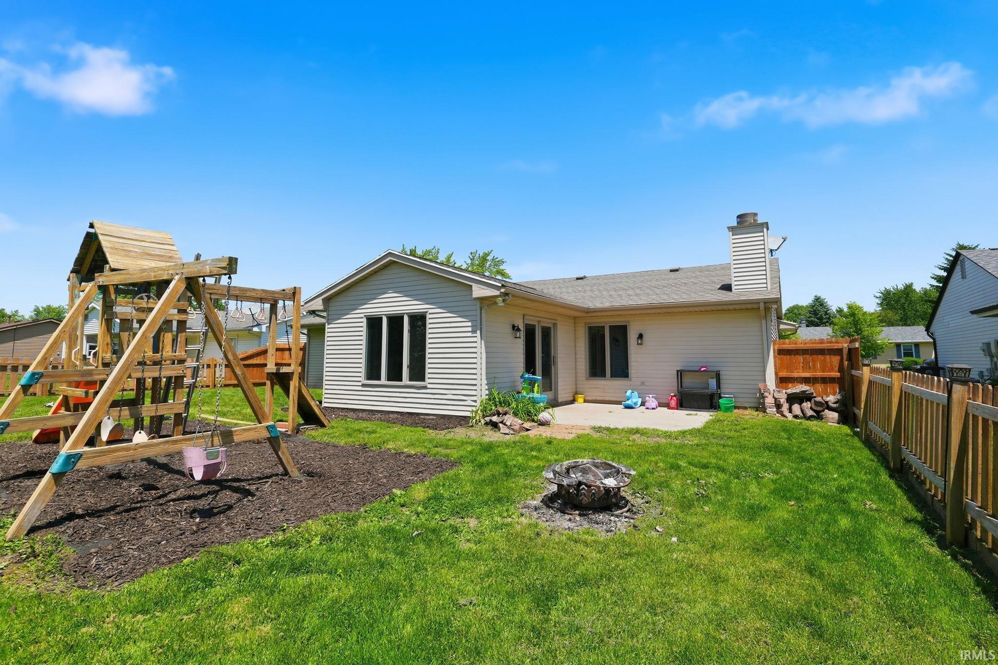 Expansive backyard featuring a concrete patio, mature green lawn, and a wood privacy fence