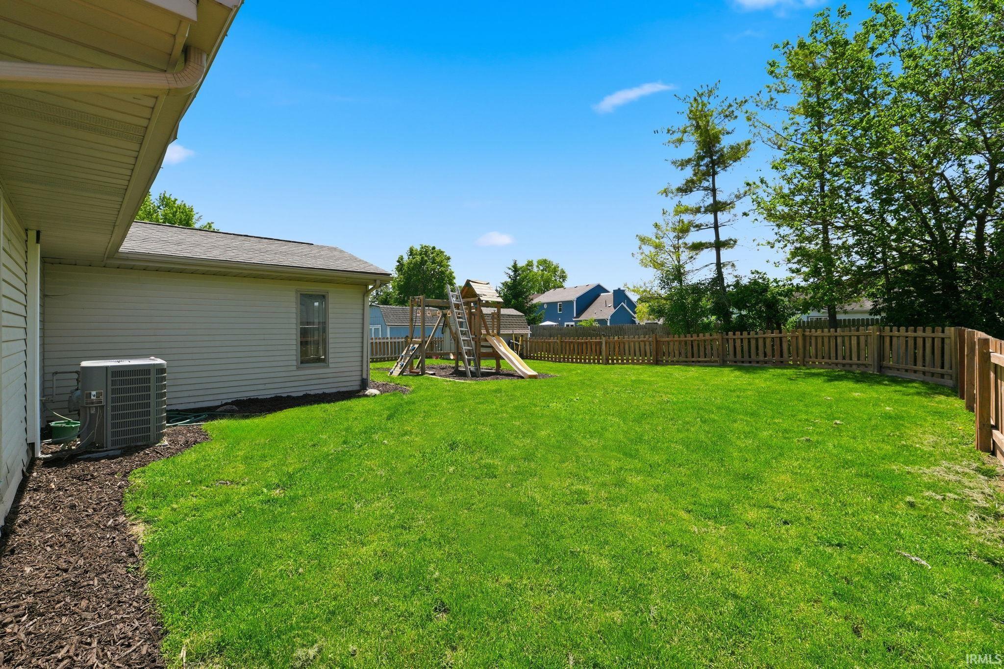 Expansive fenced backyard featuring a spacious lawn, mature trees, and a visible portion of the property's exterior siding