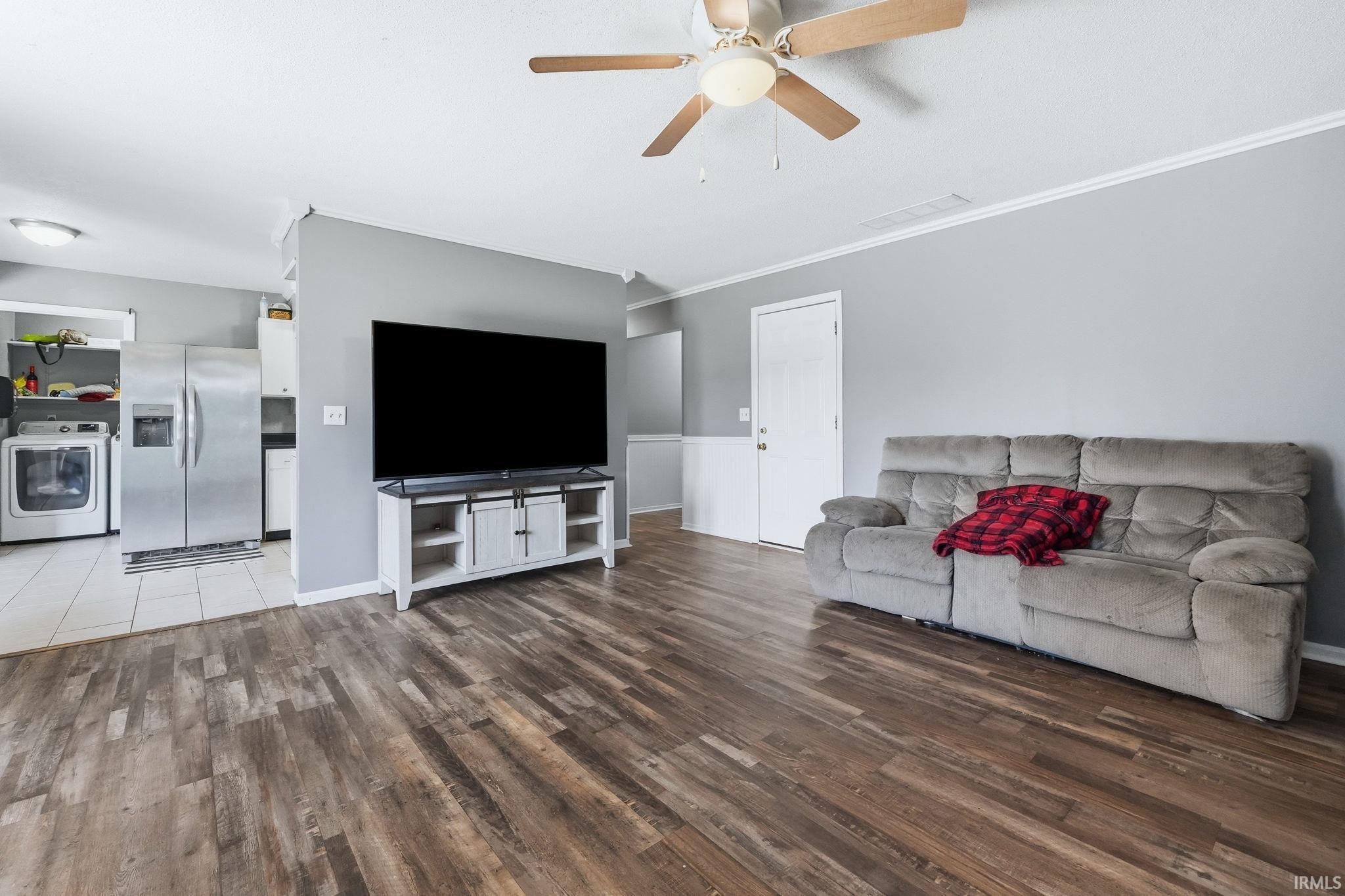 Open-concept living area featuring wood-finish flooring, a ceiling fan, and white crown molding