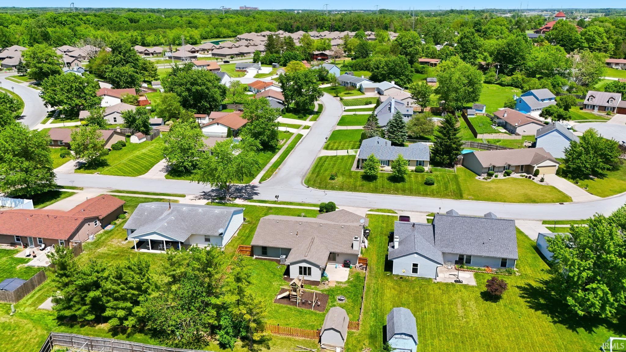 Aerial perspective showcasing a residential neighborhood with numerous single-story homes, mature trees, paved streets, and manicured lawns