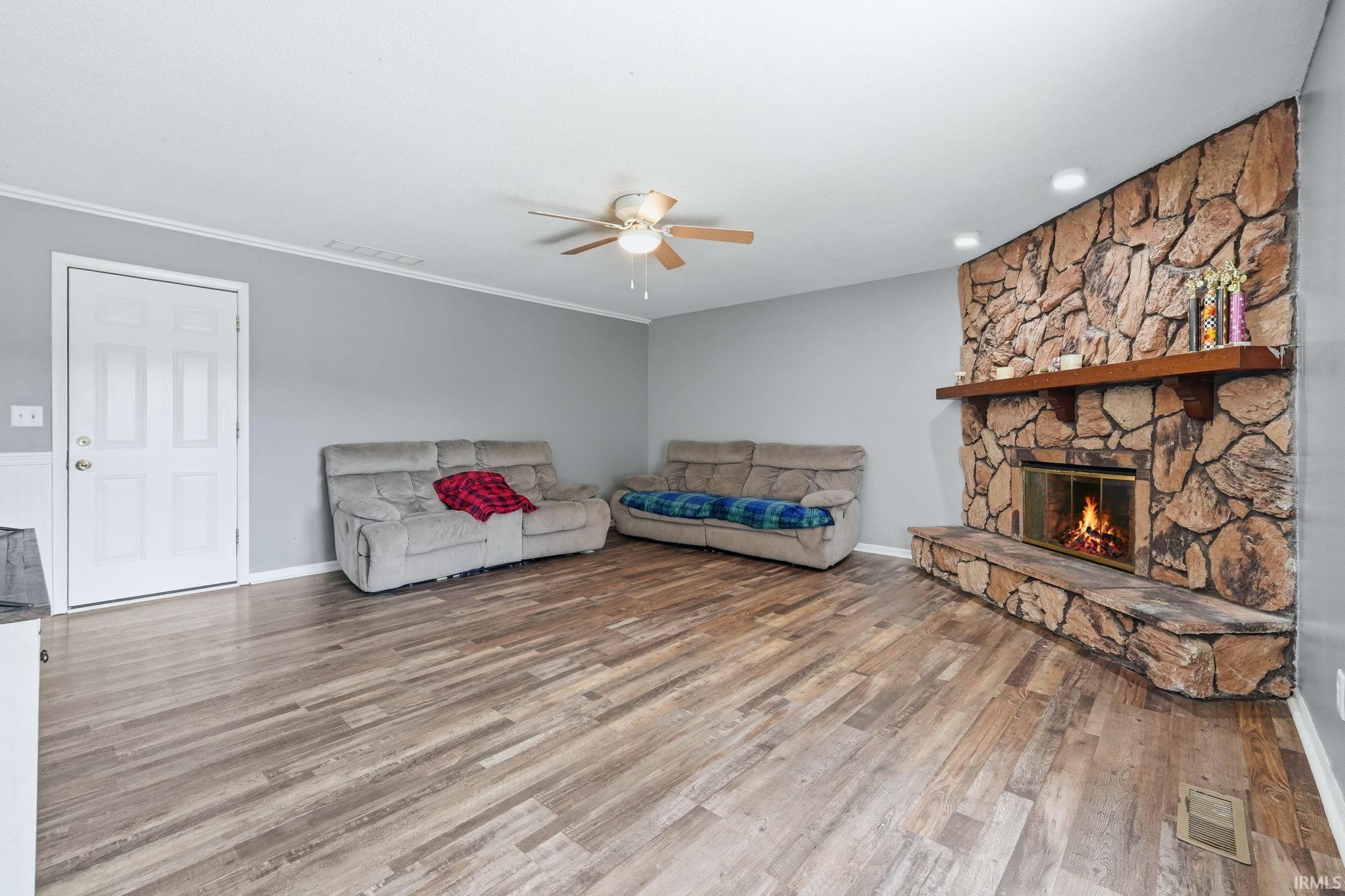 Living area featuring a stone-clad fireplace with a wood mantel, wood-finish flooring, and a ceiling fan