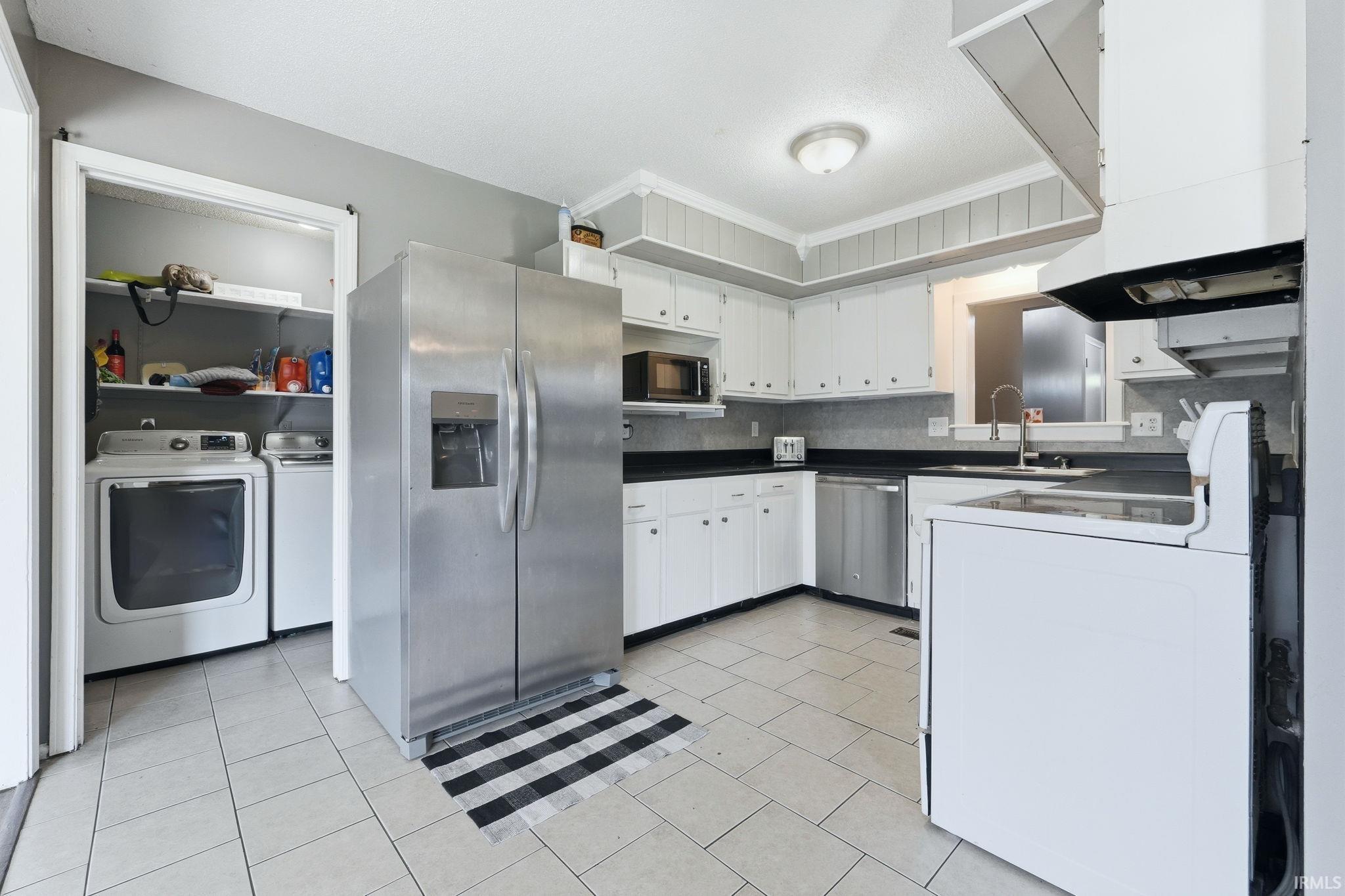 Kitchen featuring white cabinetry, dark countertops, tile flooring, and stainless steel appliances