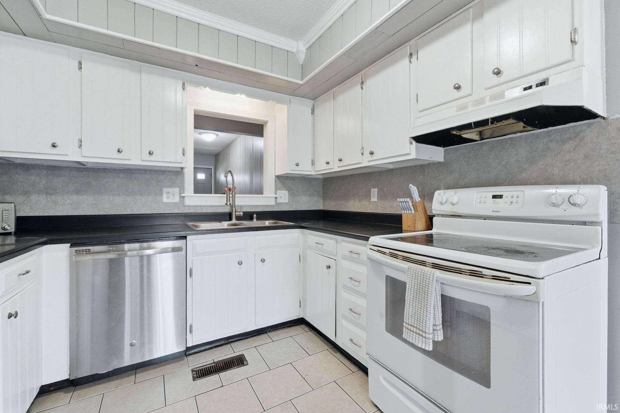 Kitchen featuring white cabinetry, black countertops, a stainless steel dishwasher, a white electric range, and light-toned tile flooring