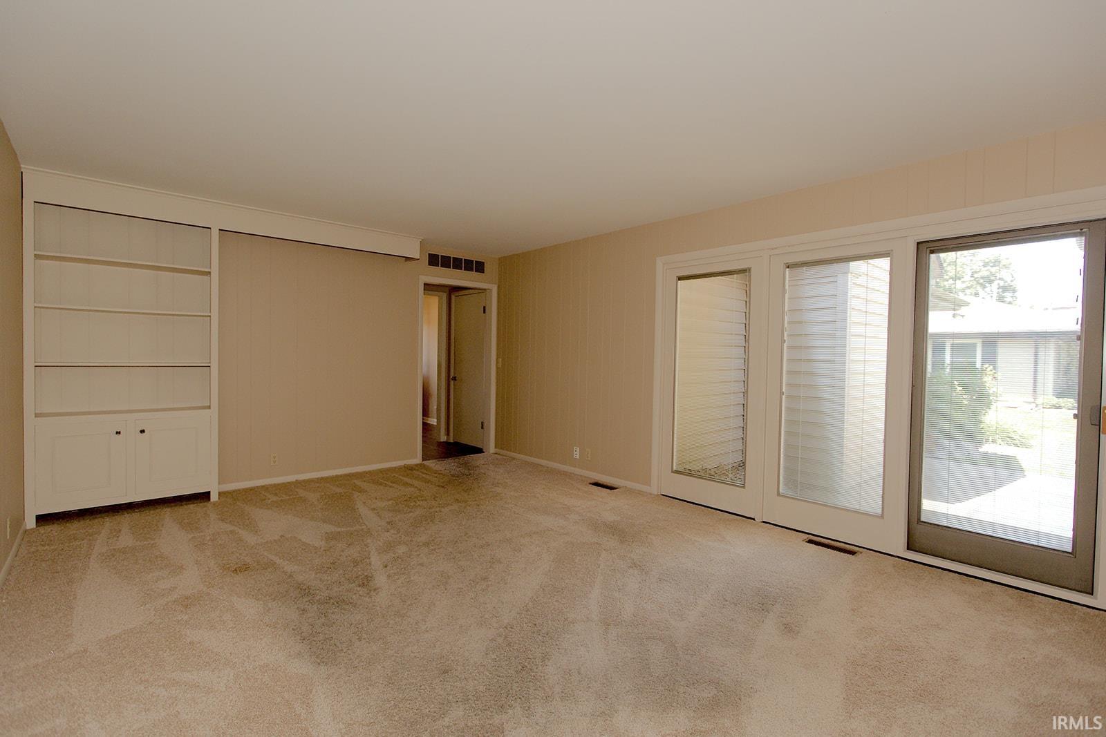 Built-in shelving with lower cabinetry, beige carpeting, neutral wall color, white trim, and a glass sliding door