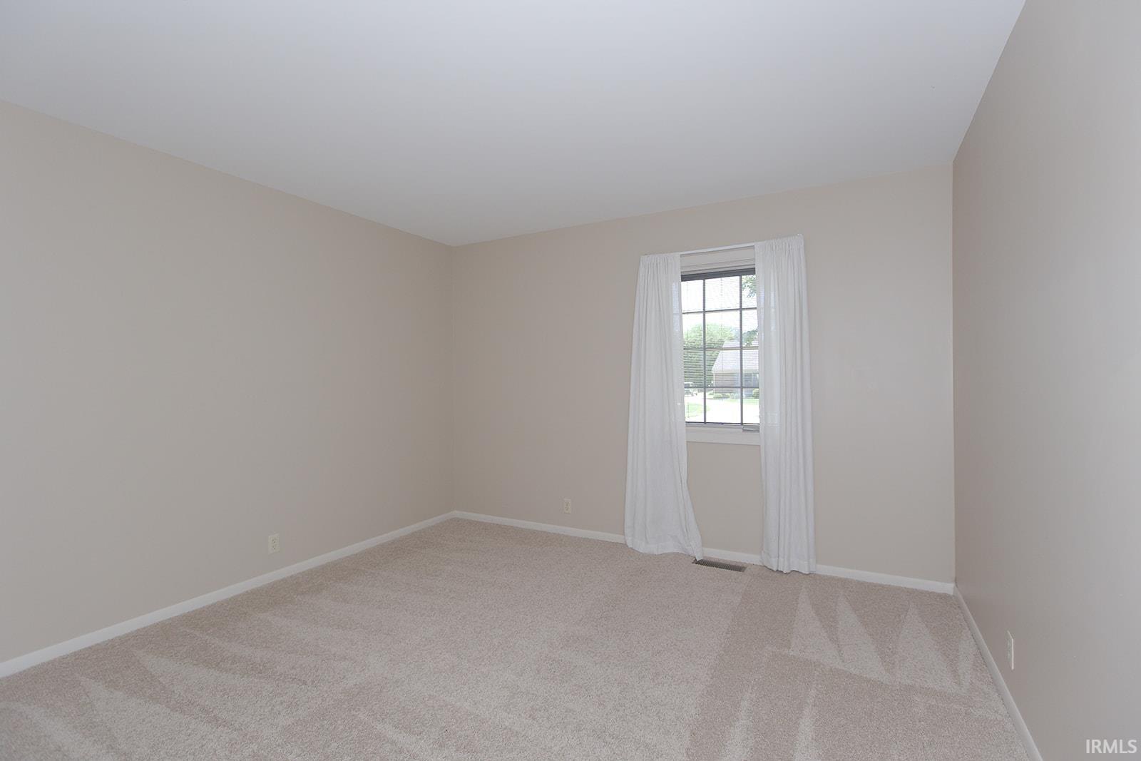 Neutral-toned room with plush carpeting, a single window featuring gridded panes, and white trim