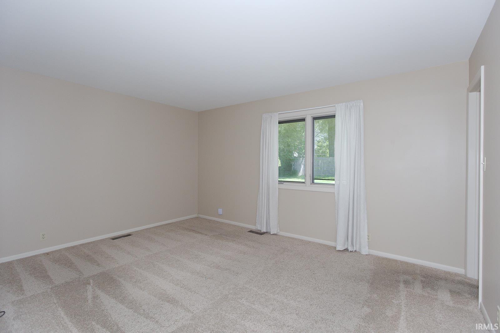 Neutral wall color, carpeted flooring, white trim, and a window with white curtains