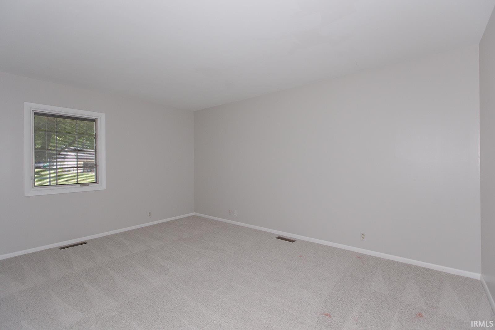 Spacious room featuring light gray walls, white baseboards, and light gray carpet