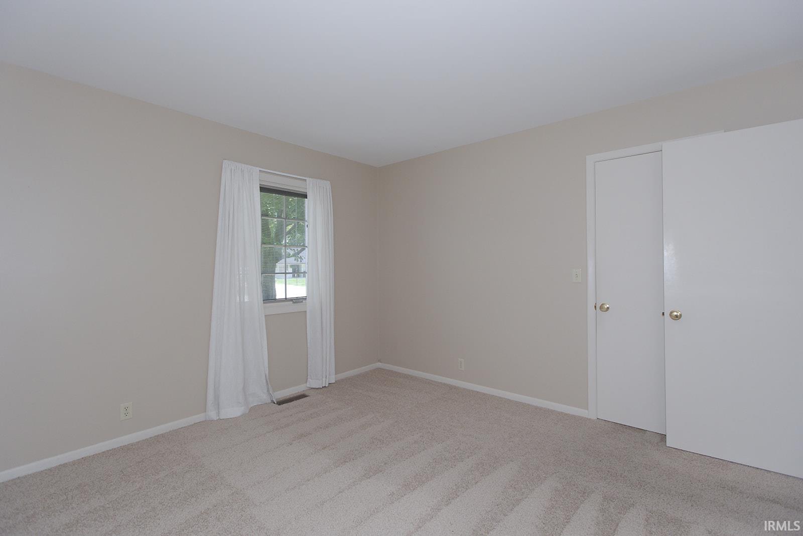 Carpeted room featuring a double sliding door closet and a single window with vertical blinds